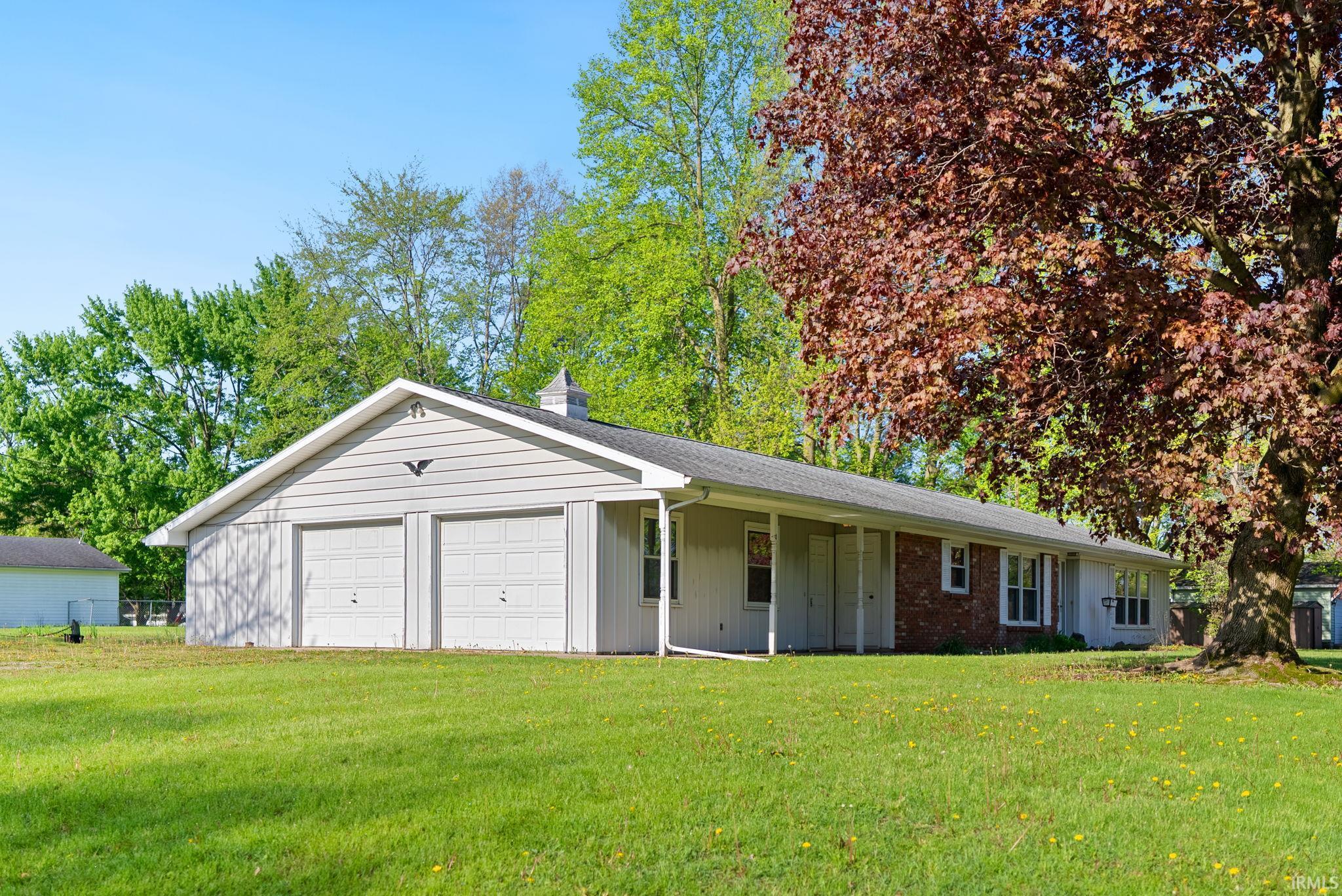 Exterior featuring a two-car garage with overhead doors, an extended covered porch, brick facade accents, and a cupola