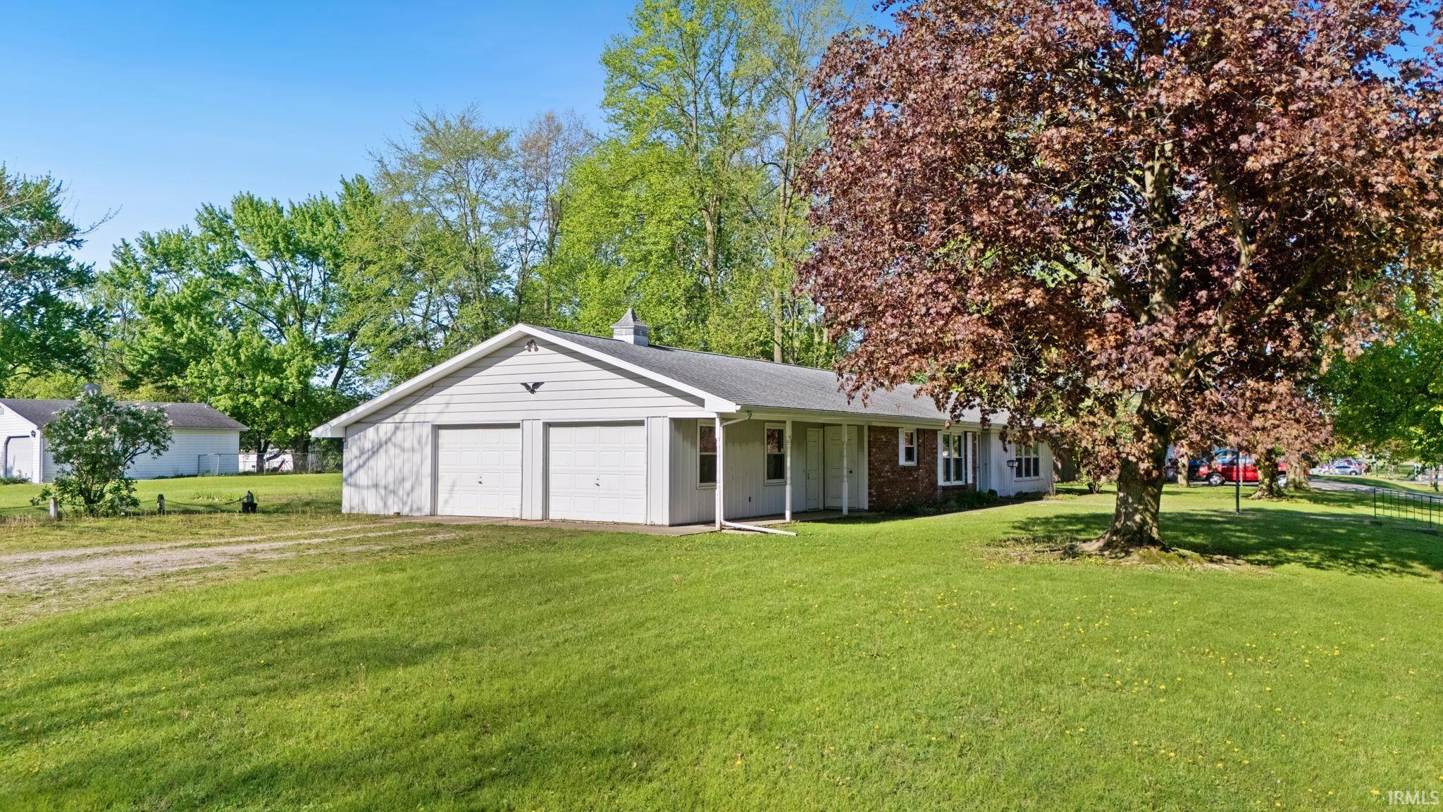 Ranch-style residence featuring a two-car attached garage with a cupola, a paved driveway, and a spacious front lawn with mature trees
