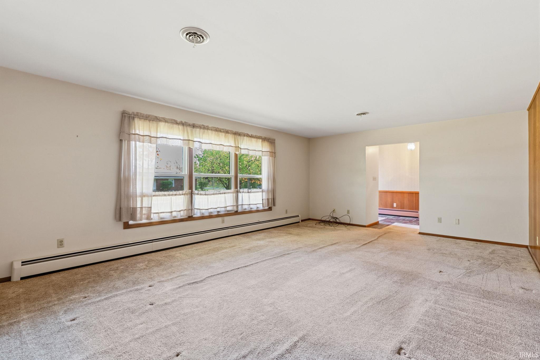 Spacious interior room featuring a large window, neutral wall paint, and baseboard heating