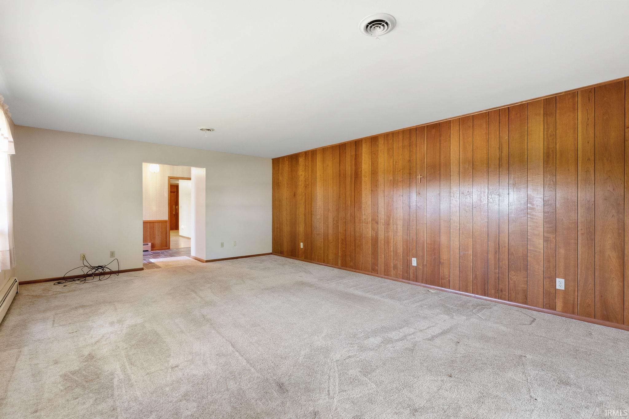 Spacious room featuring wood paneling, light-toned carpeting, and a white ceiling with a central vent
