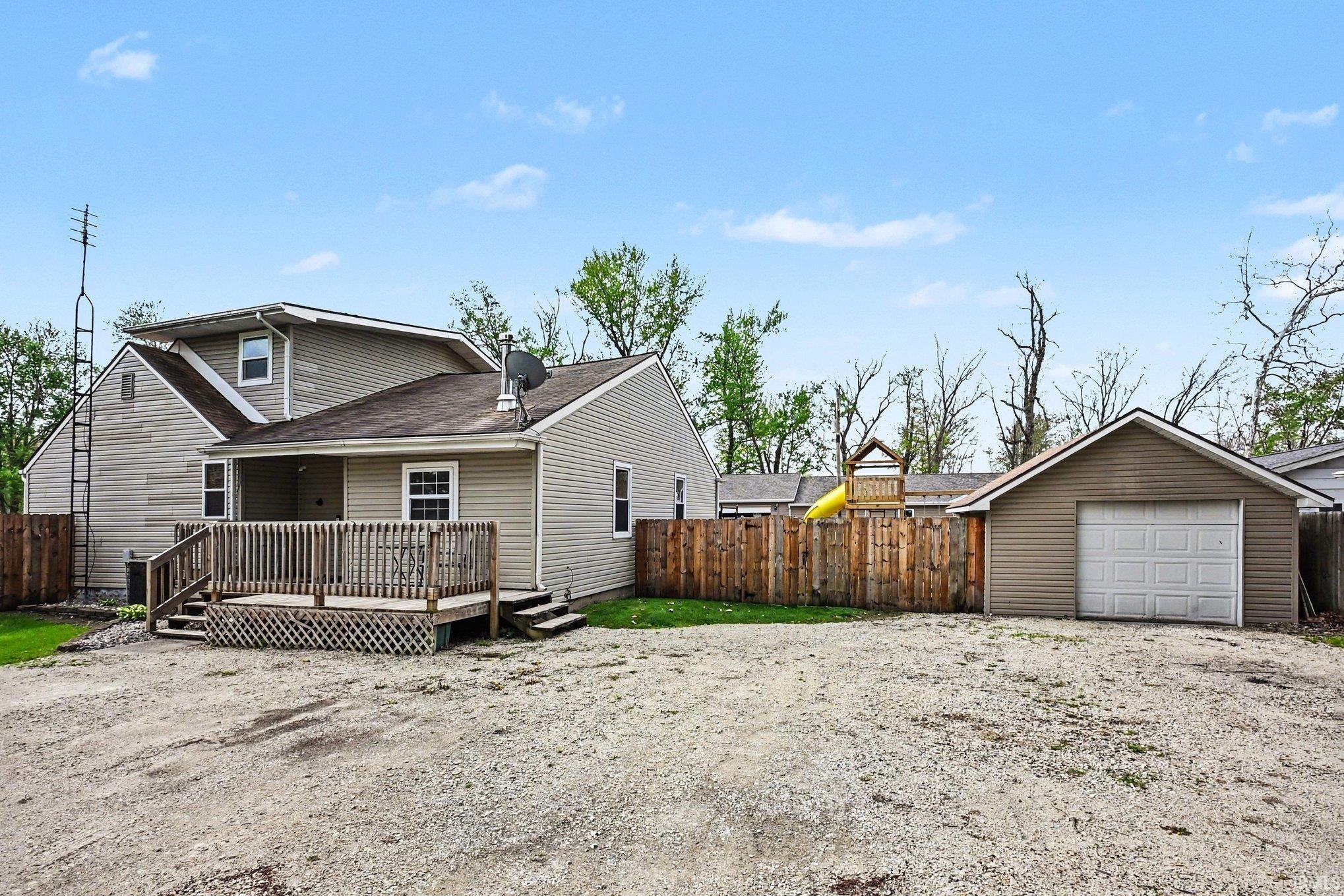 Rear exterior featuring a spacious wood deck, tan siding, and a detached single-car garage