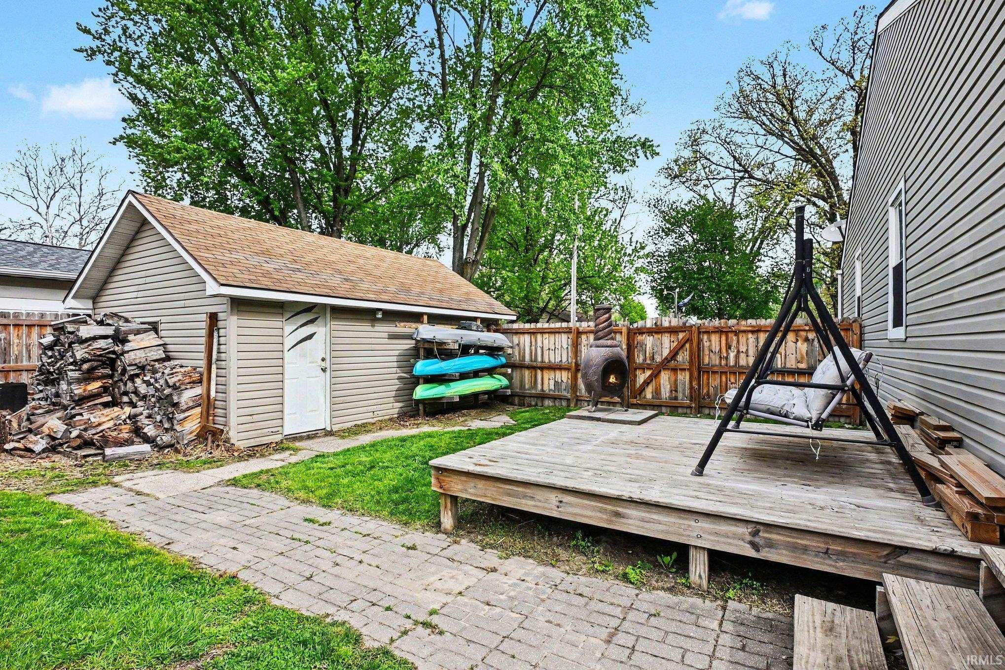 Expansive backyard featuring a wood deck, a brick paver pathway, a detached storage shed with vinyl siding, and a wood privacy fence