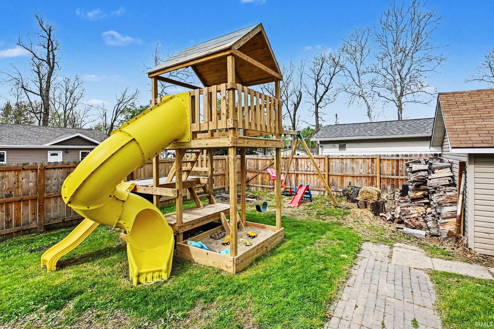 Backyard featuring a wooden playset with a yellow spiral slide, sandbox, and swing set