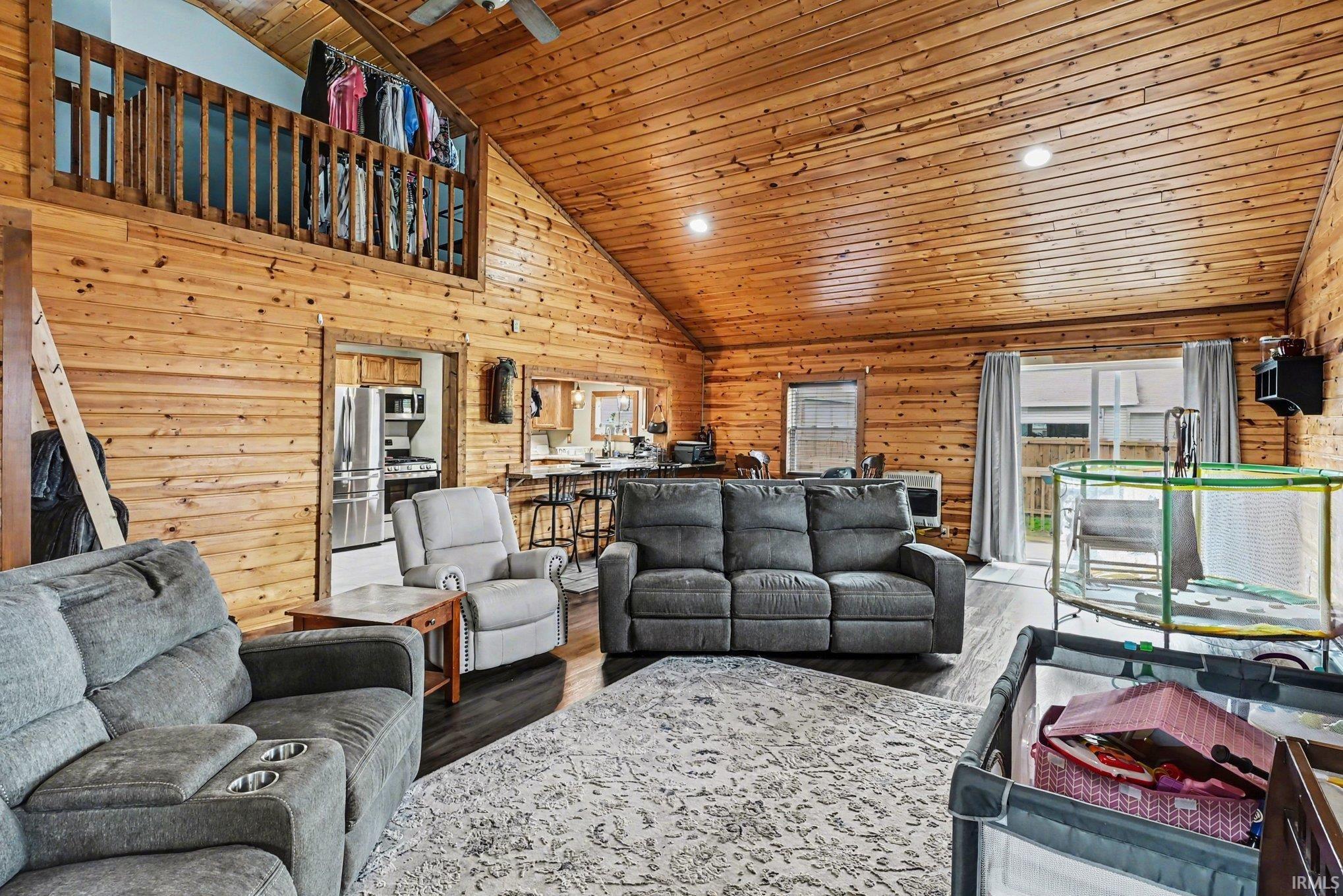 Great room featuring extensive wood-finish paneling on walls and vaulted ceilings, wood-finish flooring, and a second-story loft with a wood railing