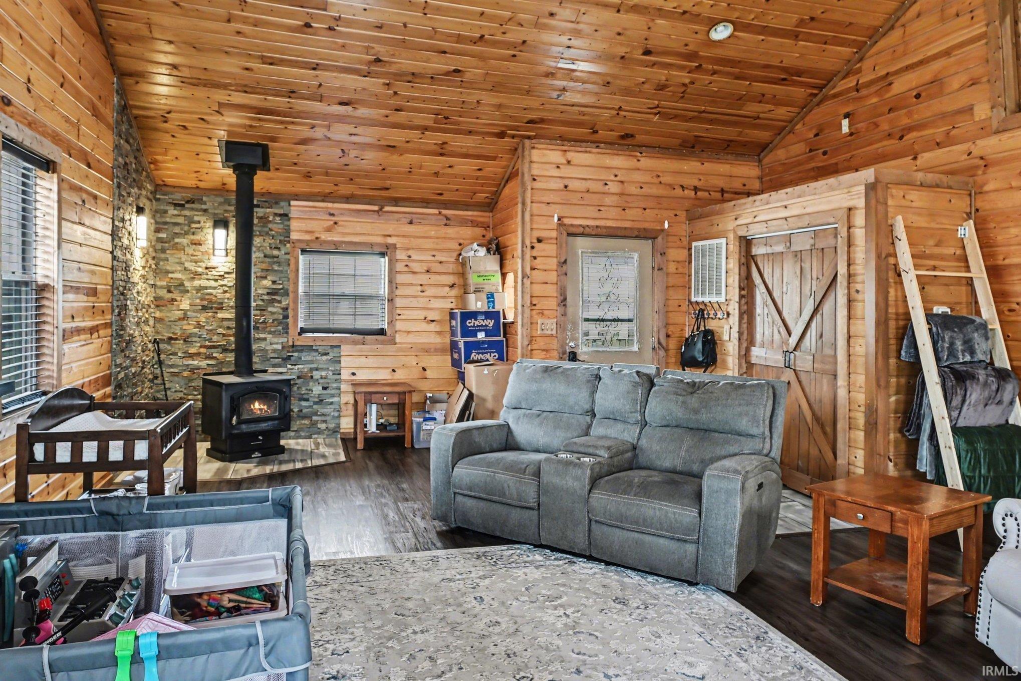 Living area featuring wood-paneled walls and ceiling, a stone accent wall, and a black wood-burning stove