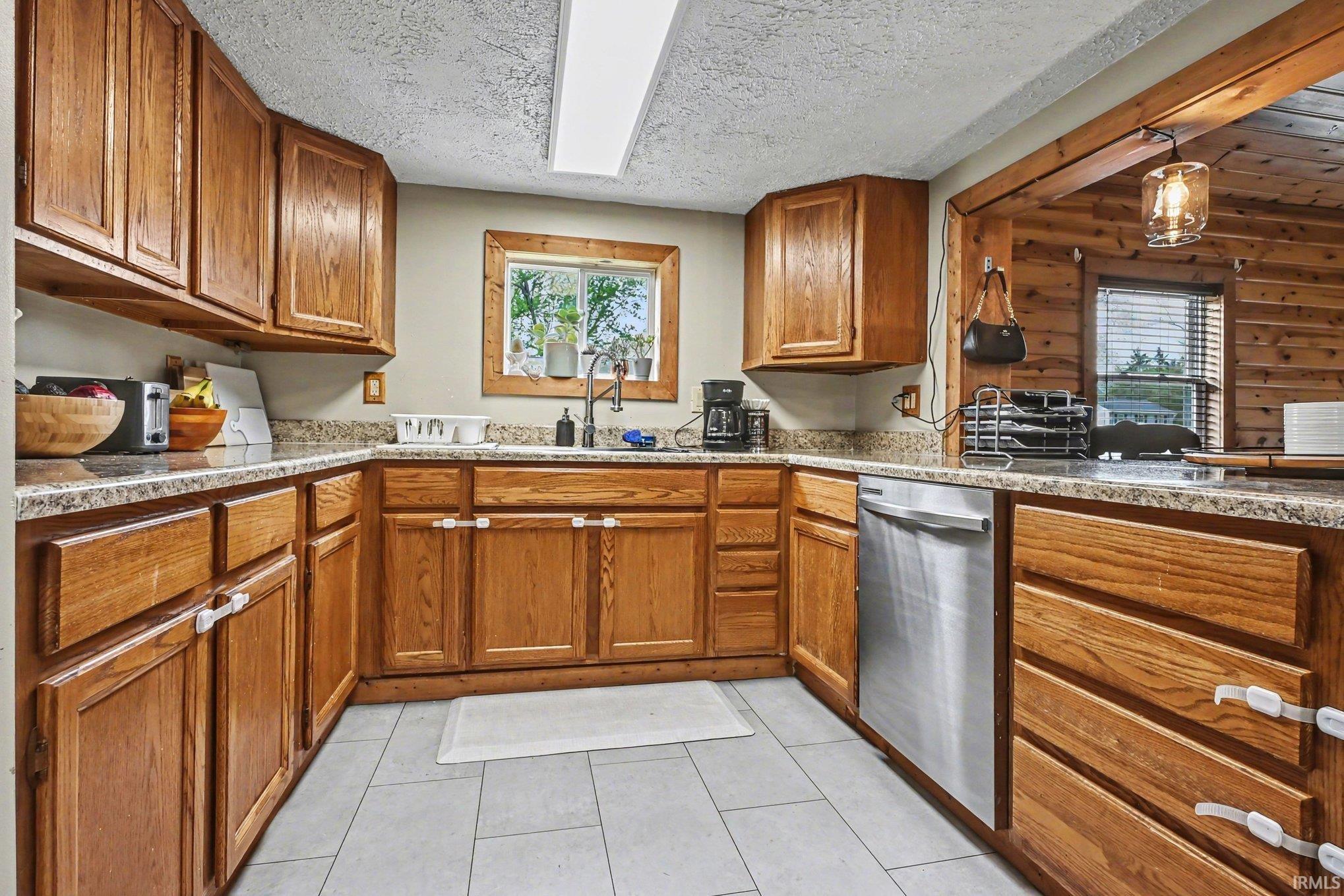 Kitchen featuring extensive wood cabinetry, light-toned countertops, a stainless steel dishwasher, and a window above the sink
