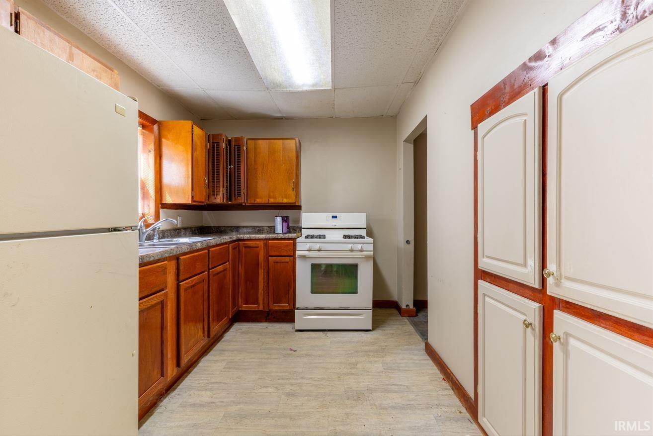Kitchen featuring wood-finish cabinetry, a white refrigerator, a white range, and built-in pantry storage with white doors and wood trim
