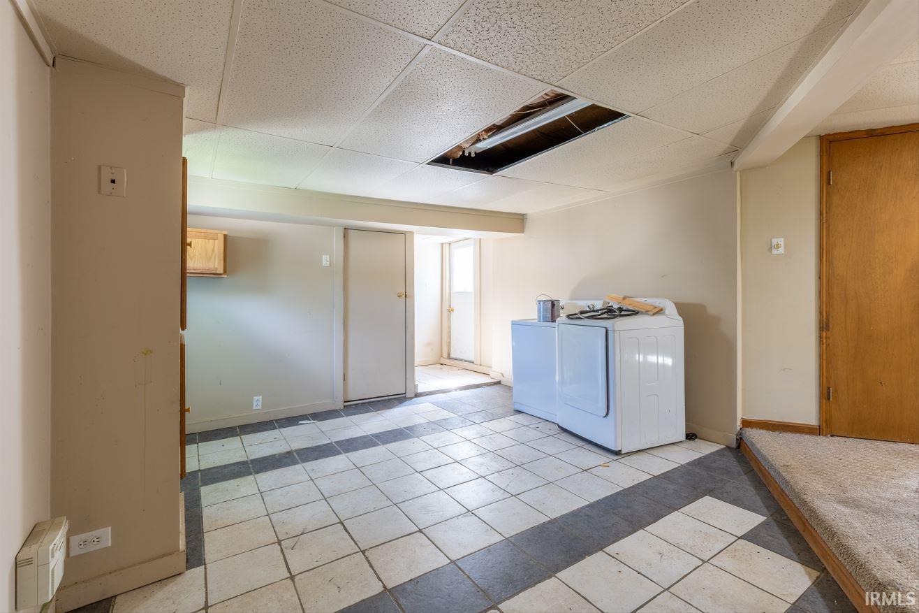 Utility room featuring a drop ceiling, a light wood-finish wall cabinet, and a tiled floor with dark contrasting accents