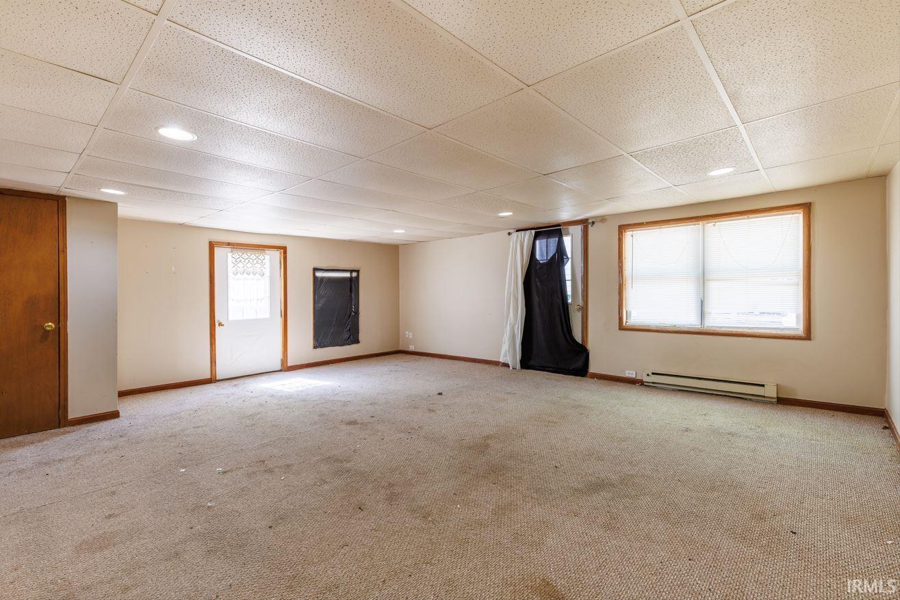 Spacious room featuring neutral carpeting, light-toned walls, and a dropped ceiling with recessed lighting
