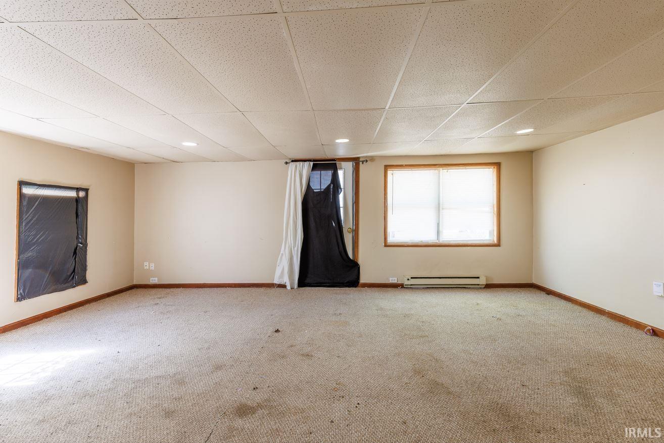 Spacious room featuring neutral painted walls, wood trim, recessed lighting, and a drop ceiling
