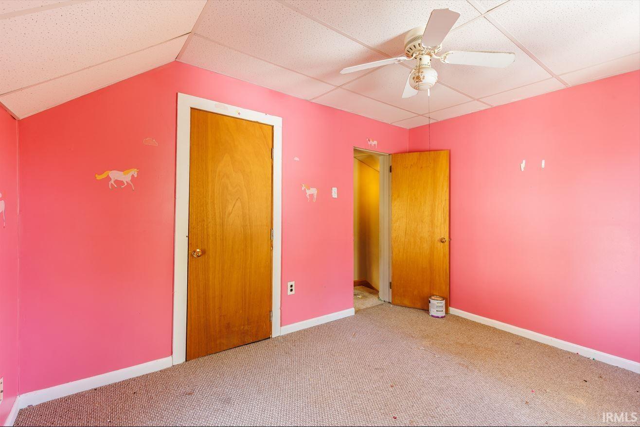 Room featuring sloped ceilings, two wooden panel doors, and a ceiling fan