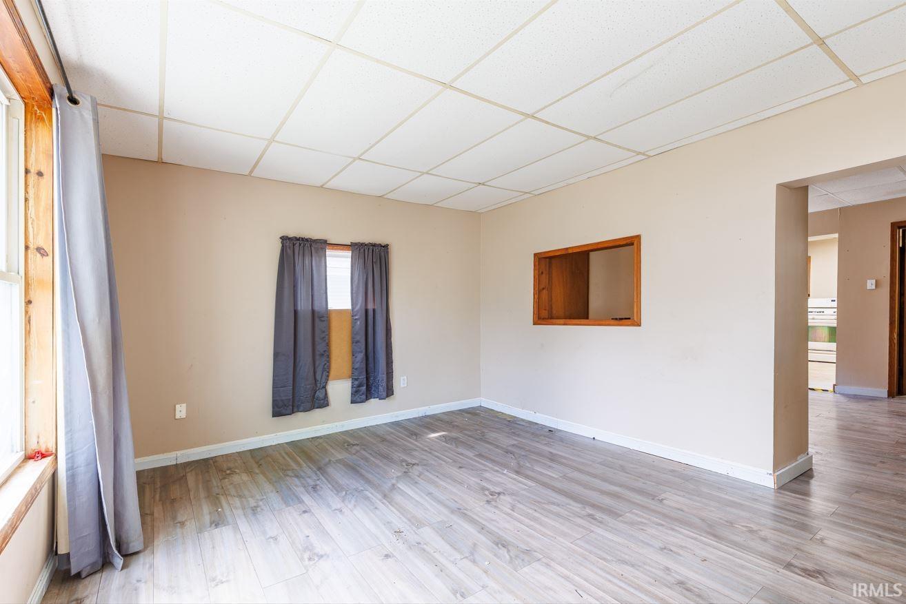 Spacious room featuring wood-finish flooring, neutral wall tones, two windows with natural wood trim, and a ceiling with acoustic tiles