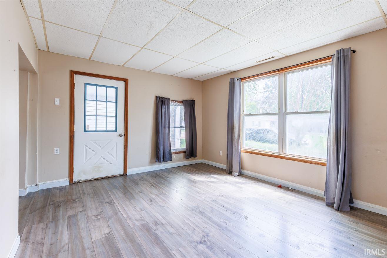 Spacious room featuring wood-finish flooring, neutral-toned walls, and a dropped ceiling