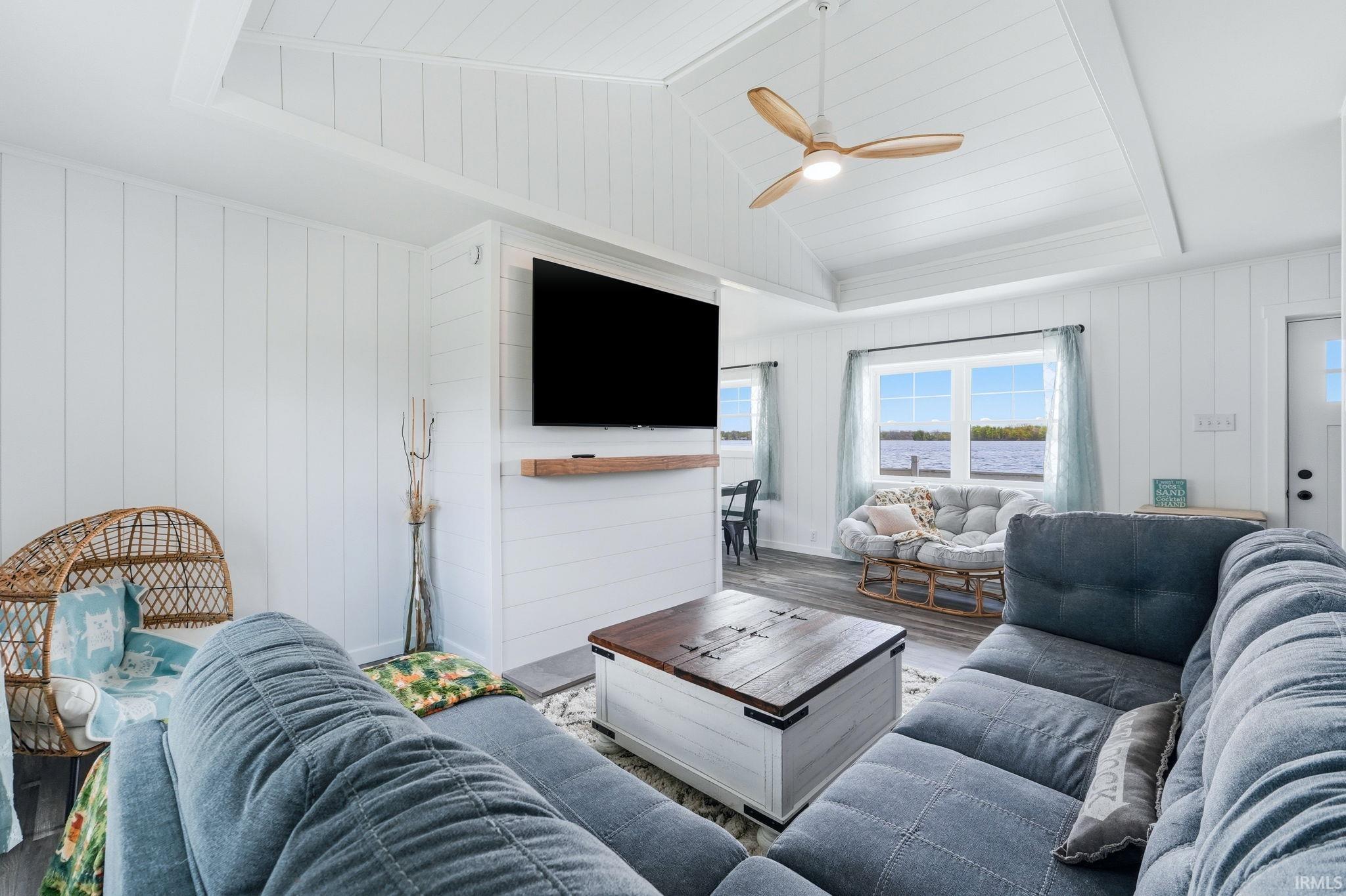 Vaulted planked ceiling with exposed beams and a ceiling fan, white paneled walls, and wood-finish flooring