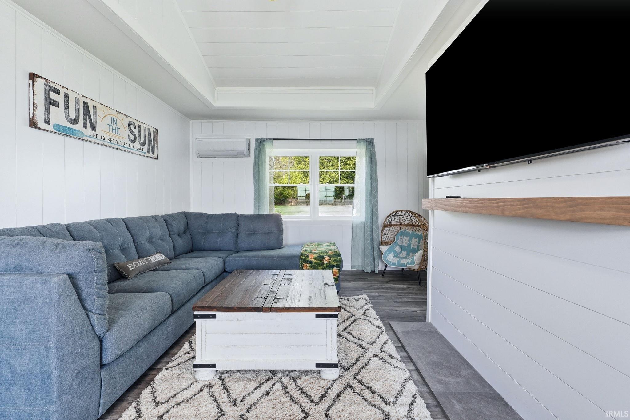 Living area featuring a tray ceiling, shiplap wall accents, and wood-finish flooring