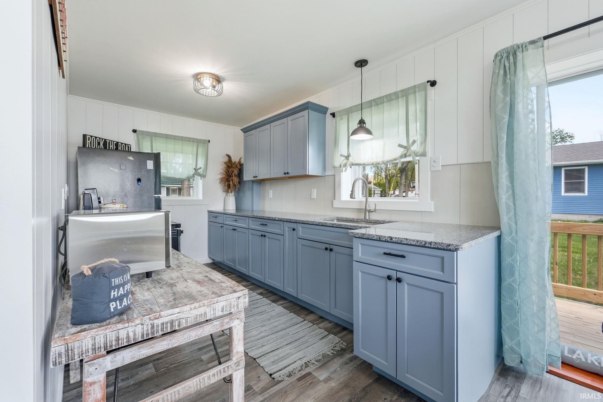 Kitchen featuring light blue cabinetry, granite countertops, a stainless steel sink with a gooseneck faucet, light gray subway tile backsplash, and wood-finish flooring