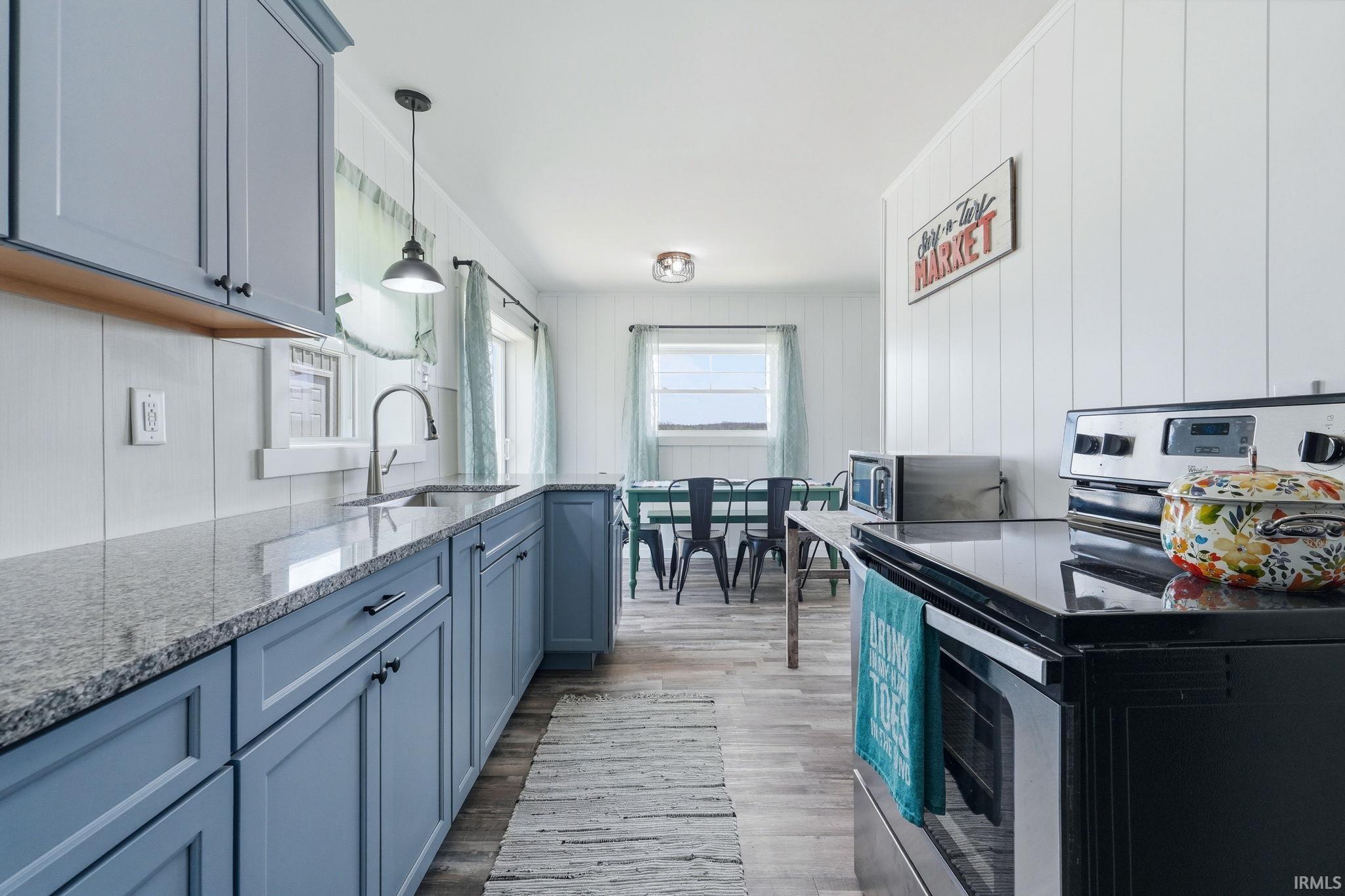 Modern kitchen featuring light blue cabinetry with dark hardware, granite-style countertops, and a stainless steel sink with a gooseneck faucet
