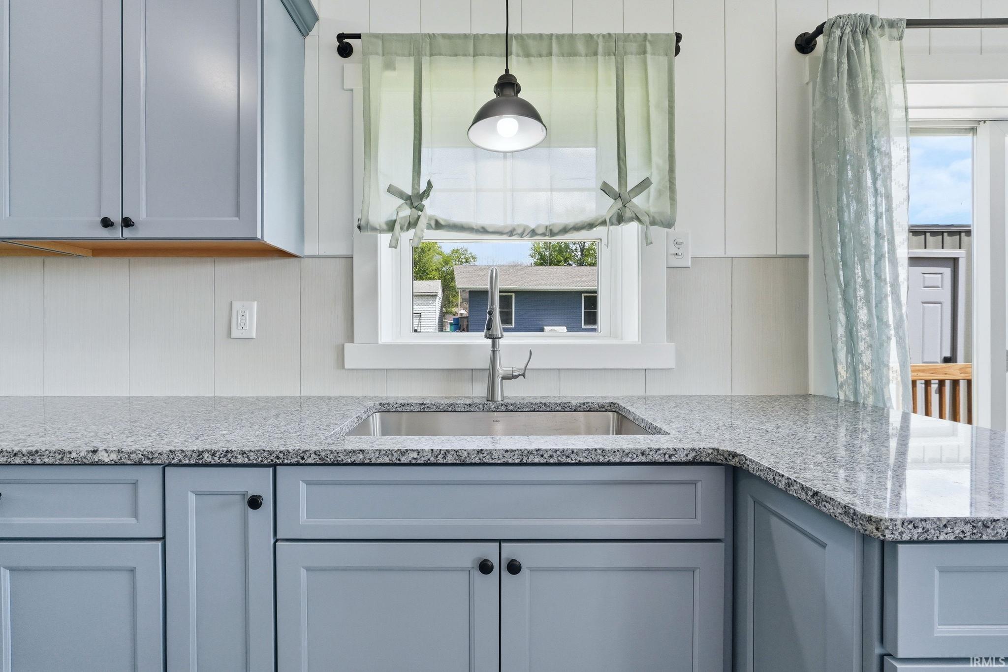 Kitchen featuring light blue shaker-style cabinetry, speckled countertops, a stainless steel undermount sink, and a gooseneck faucet