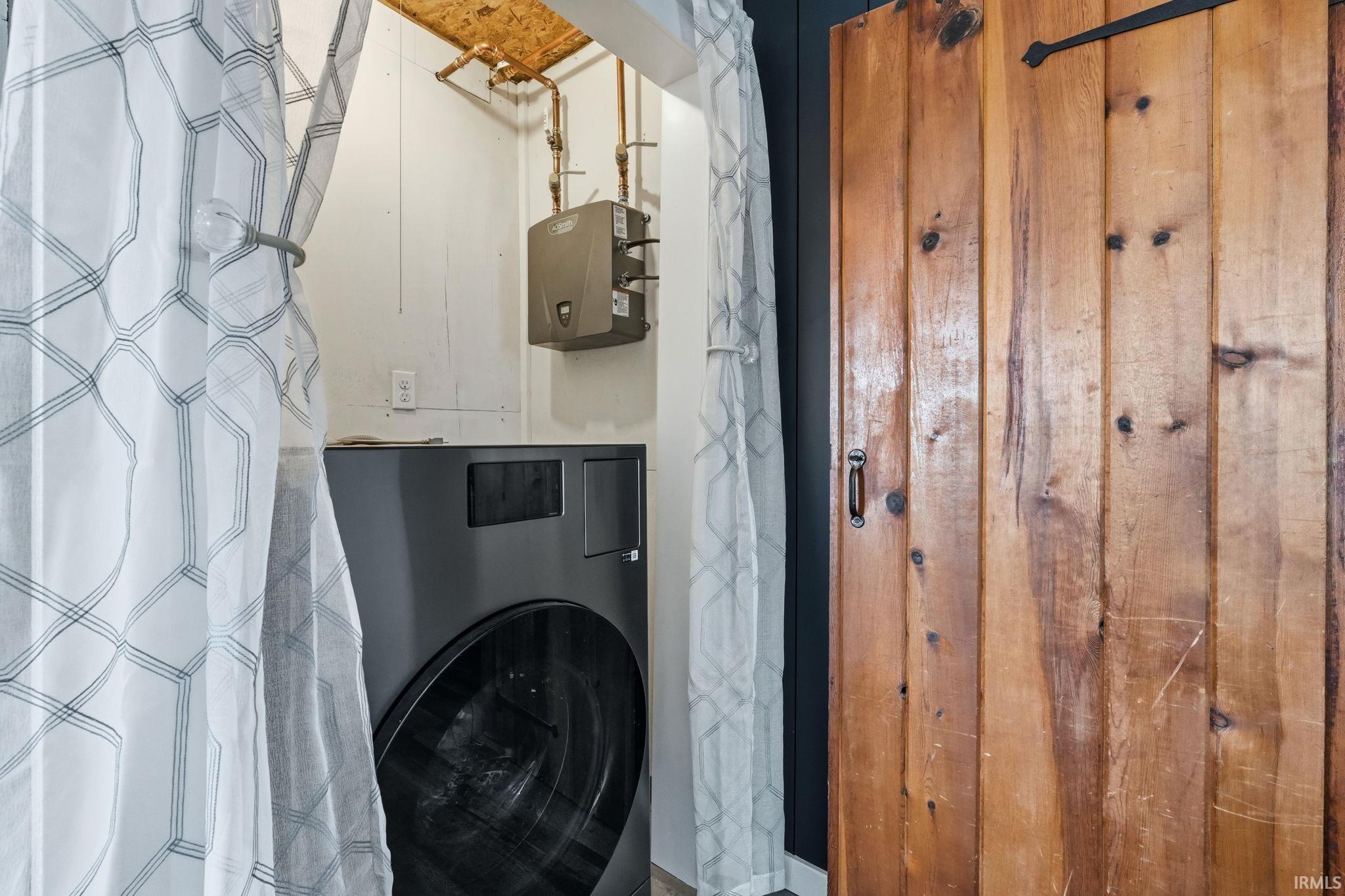 Dedicated utility area featuring a front-load washer, wall-mounted water heater, exposed copper piping, and a wood-finish barn door