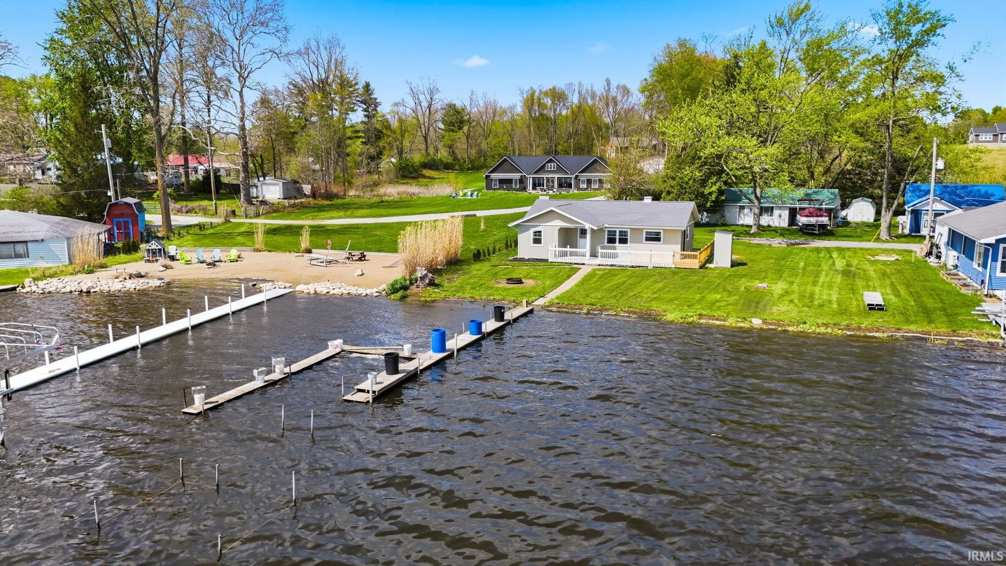Waterfront property featuring a private dock system, a sandy beach area, and a gently sloping grassy yard leading to the water