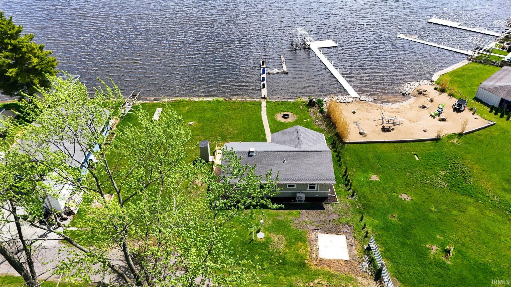 Waterfront property featuring extensive shoreline access, a private dock, manicured lawn, and sandy beach area