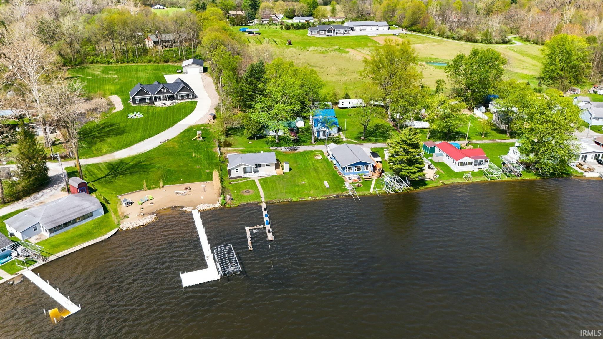 Waterfront property featuring a private dock, expansive green lawn, and a sandy beach area