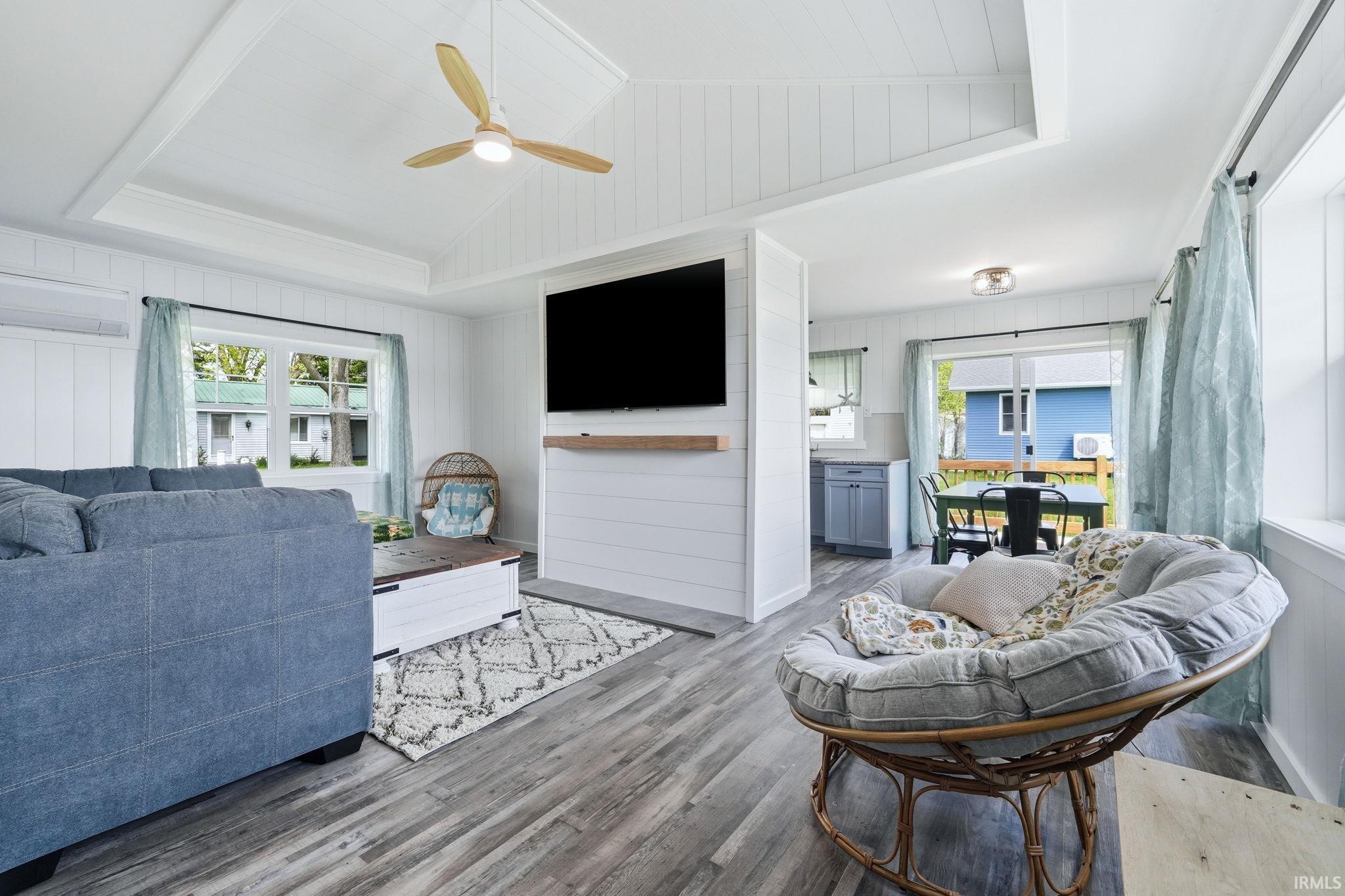Living area featuring a vaulted ceiling with exposed beams, a ceiling fan with integrated lighting, wood-finish flooring, and white shiplap walls
