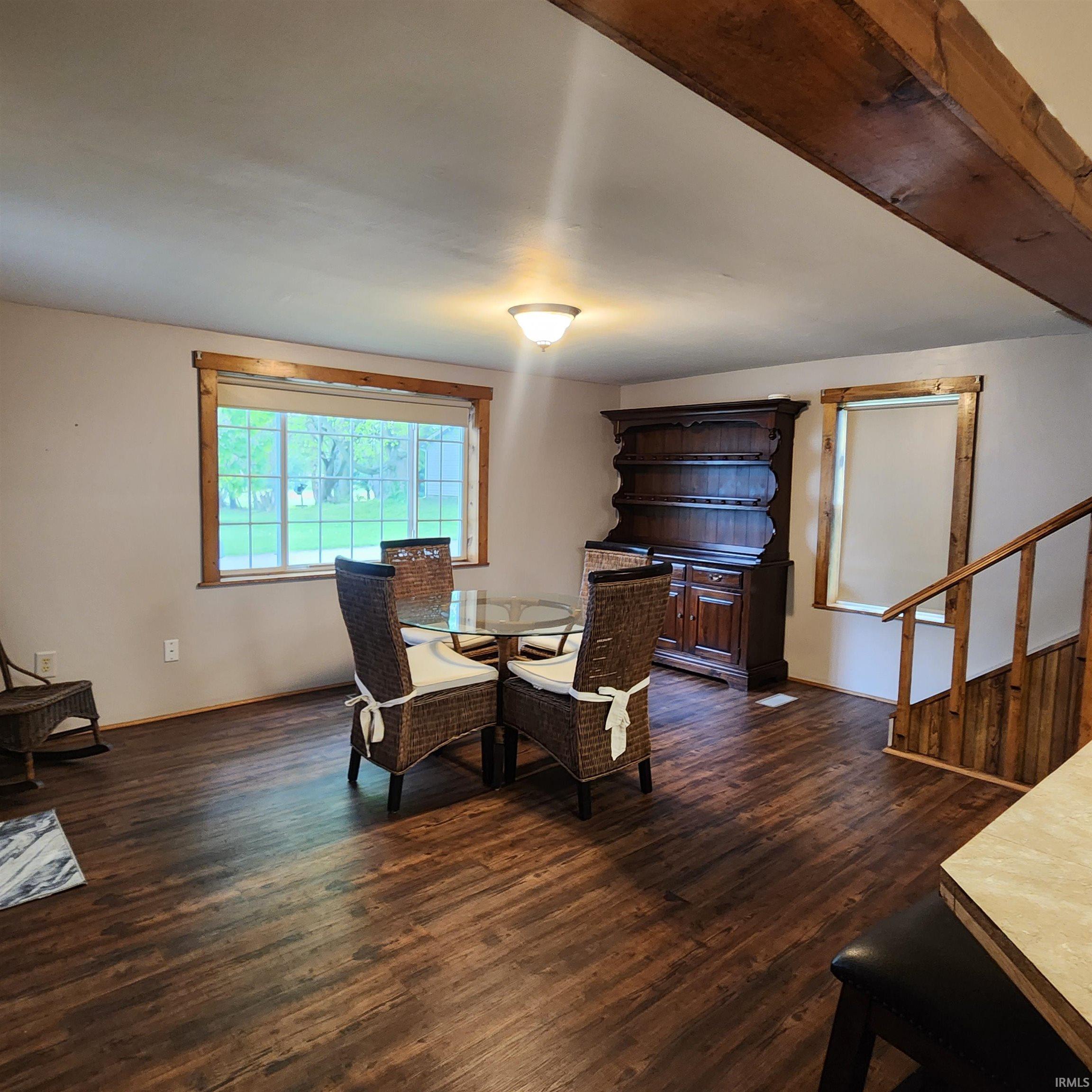 Open-concept living space featuring wood-finish flooring, exposed ceiling beams, a large picture window, and natural wood trim throughout