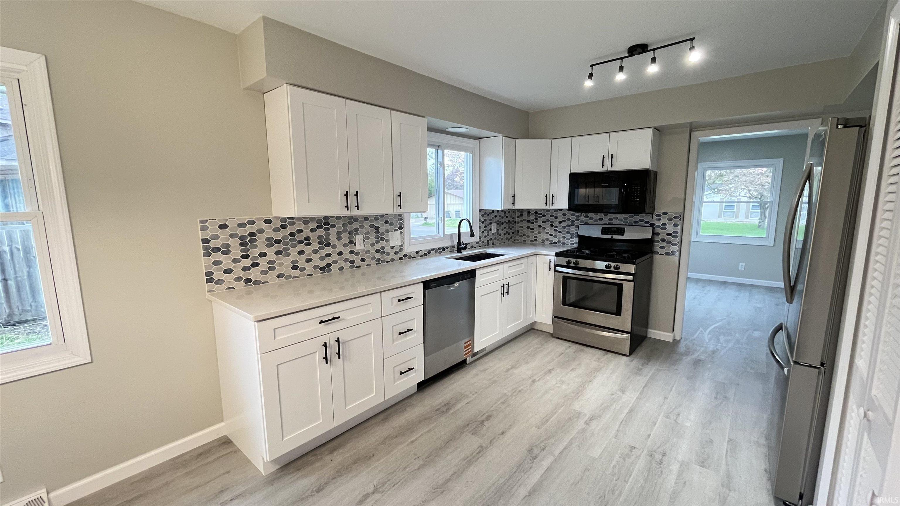 Kitchen featuring white shaker cabinetry, patterned tile backsplash, stainless steel appliances, light wood-finish flooring, and track lighting