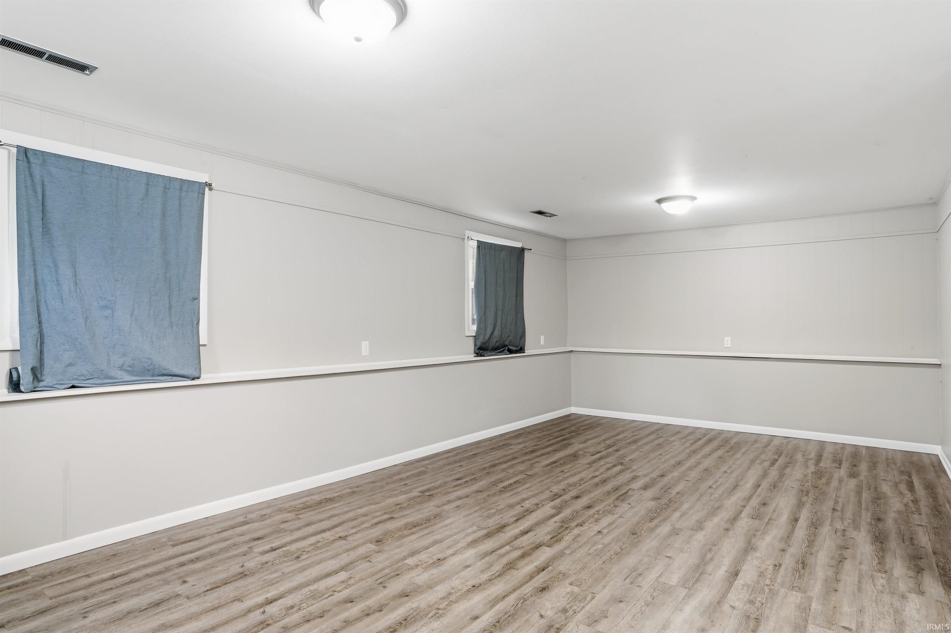 Spacious room featuring wood-finish flooring, light grey walls, white trim, and two flush-mount ceiling lights