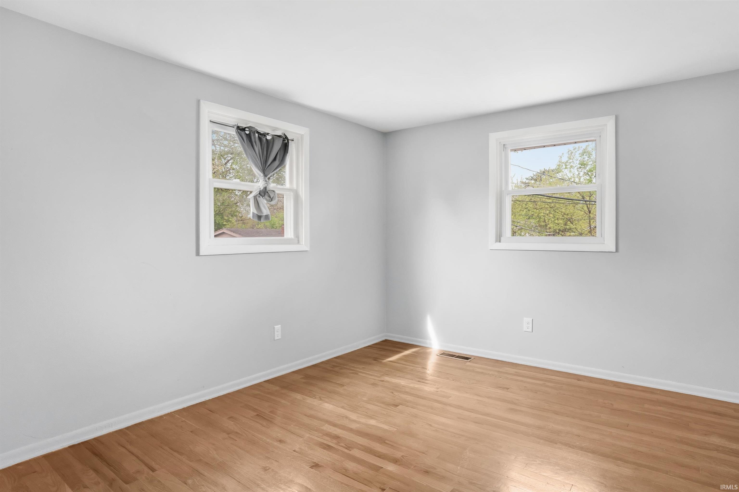 Spacious room featuring light-toned walls, wood-finish flooring, and white trim