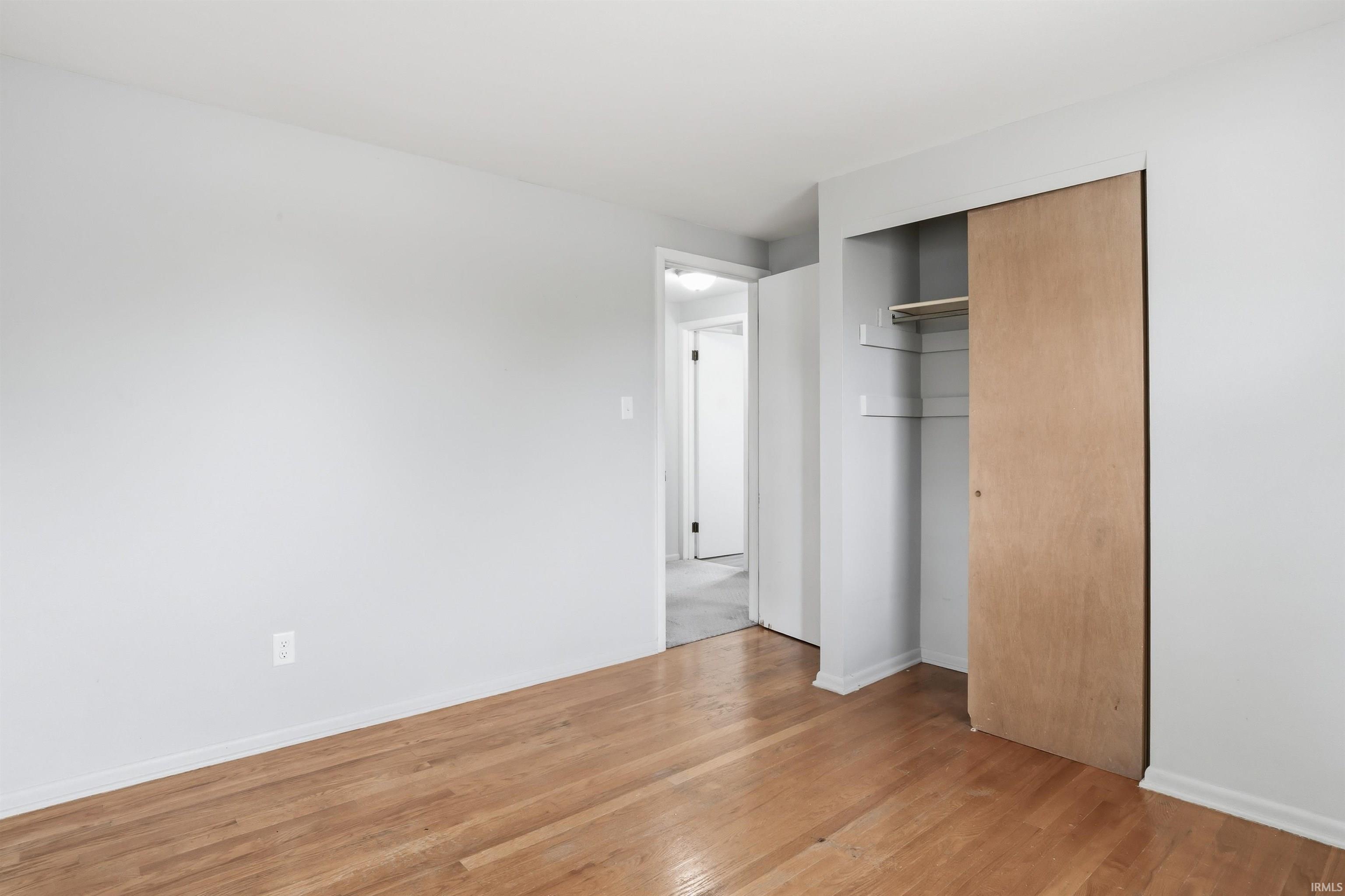 Bedroom featuring wood-finish flooring, light grey painted walls, white baseboards, and a built-in closet with sliding wood doors and interior shelving