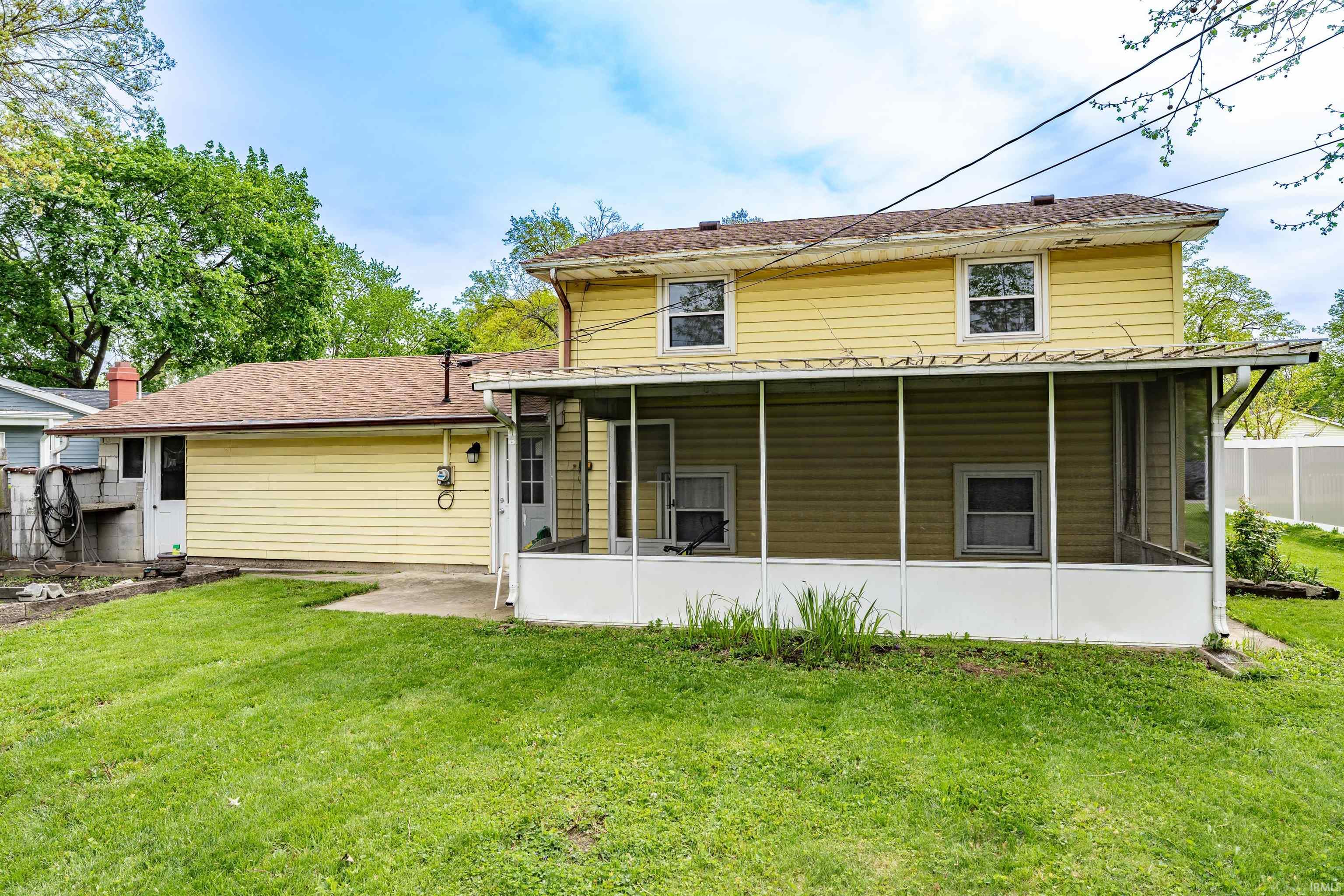 Rear exterior featuring yellow siding, a screened porch, and a concrete patio