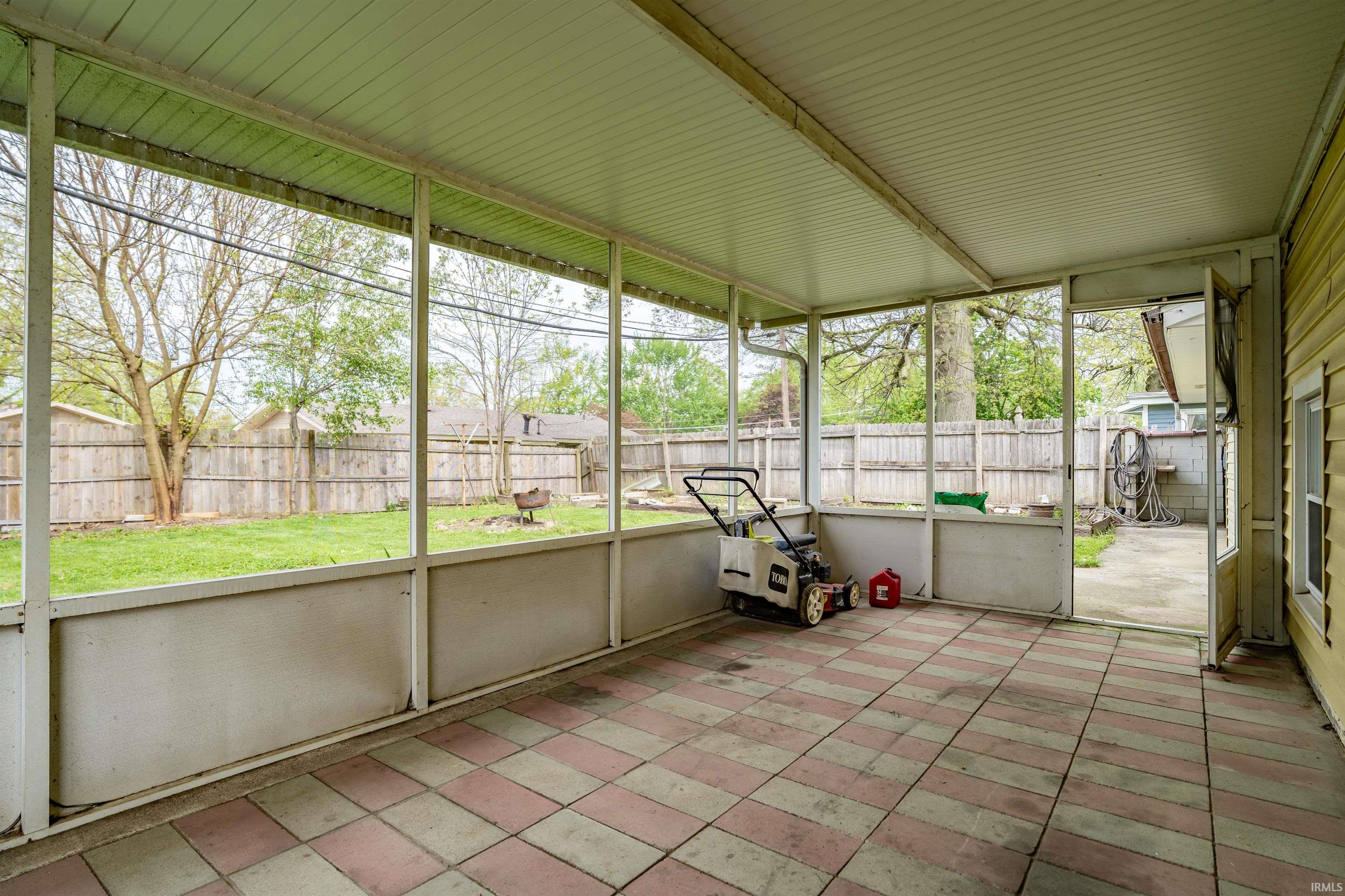 Screened porch with a tiled floor, overlooking a fenced backyard with a grass lawn