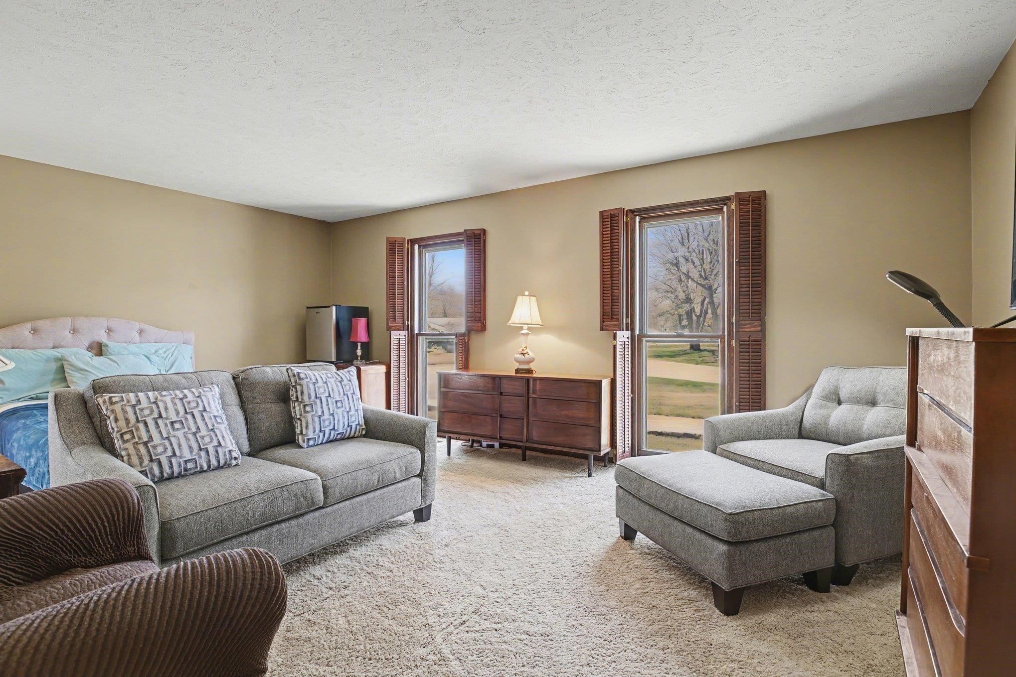 Carpeted room with neutral-toned walls, featuring two windows with louvered shutters