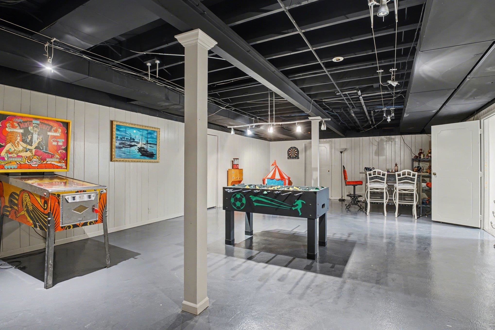 Expansive finished basement featuring white vertical paneling and a dark painted exposed beam ceiling with track lighting