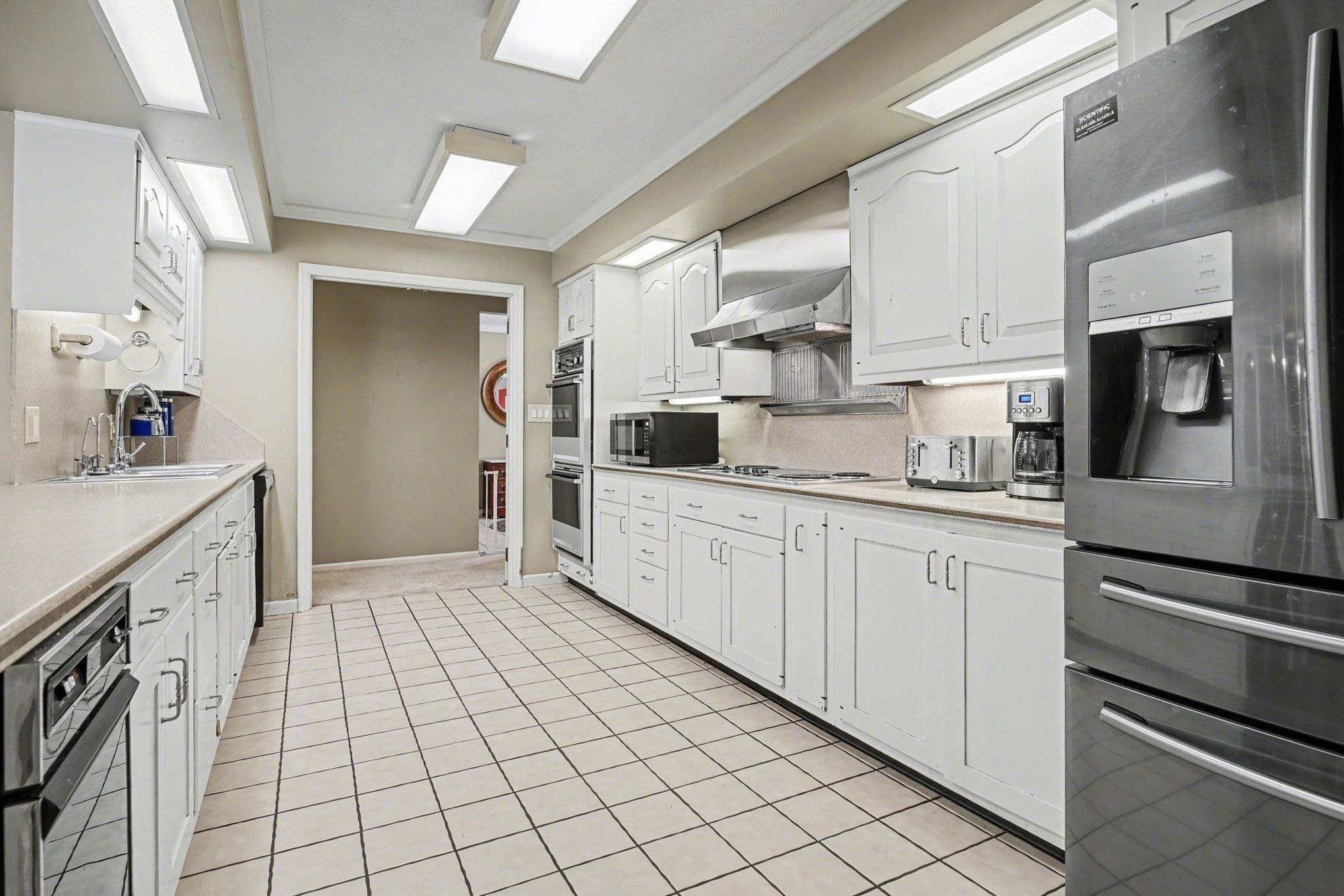 Galley kitchen featuring extensive white cabinetry, light-toned tile flooring, stainless steel appliances, and recessed ceiling lighting