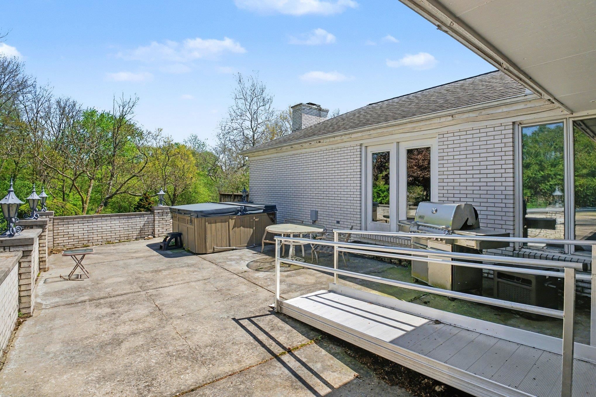 Paved patio featuring a built-in hot tub, brick privacy wall, exterior lighting fixtures, and direct access to interior spaces through glass doors