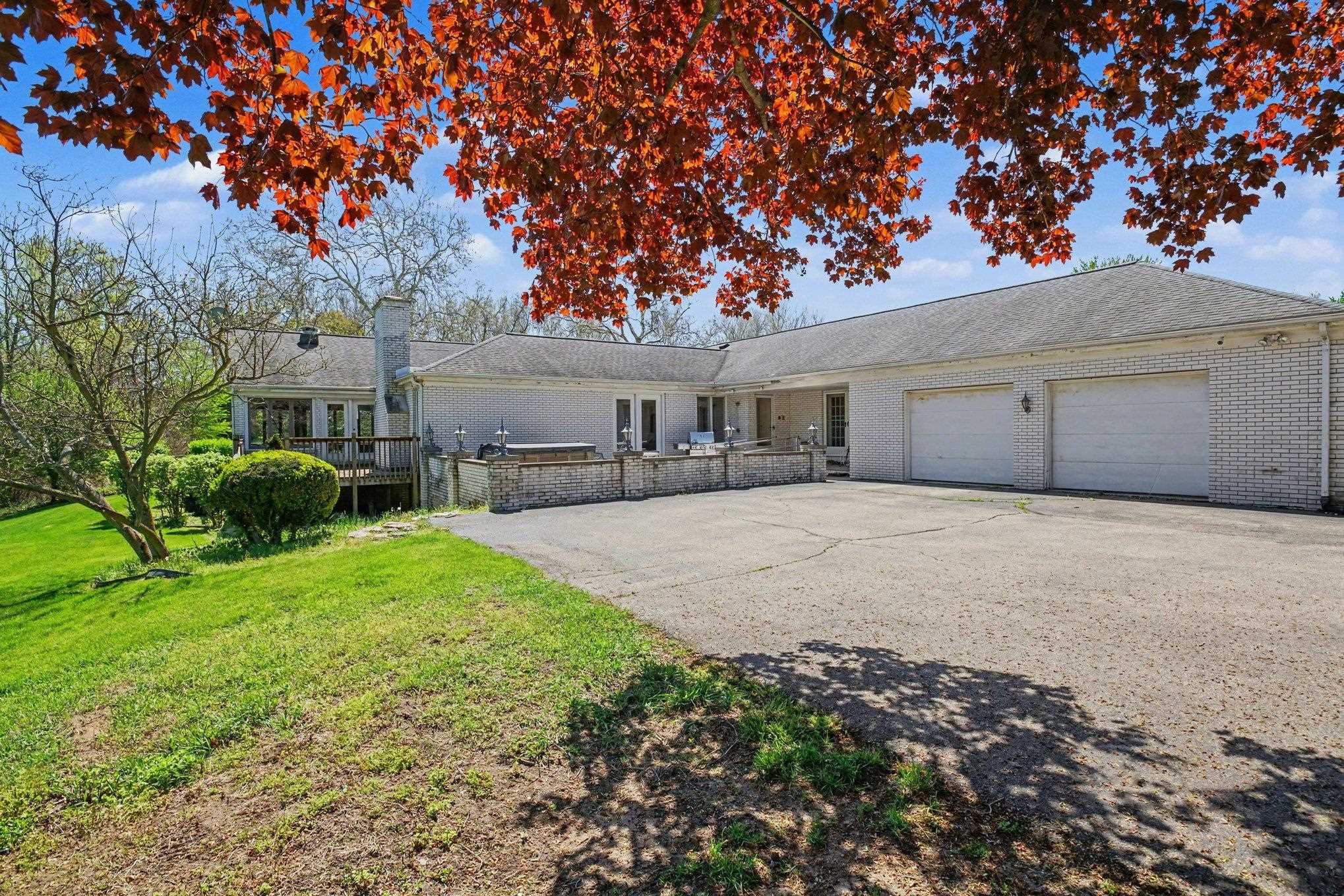 Spacious property featuring a light brick exterior, a multi-car garage with two white doors, a large paved driveway, and a wood deck