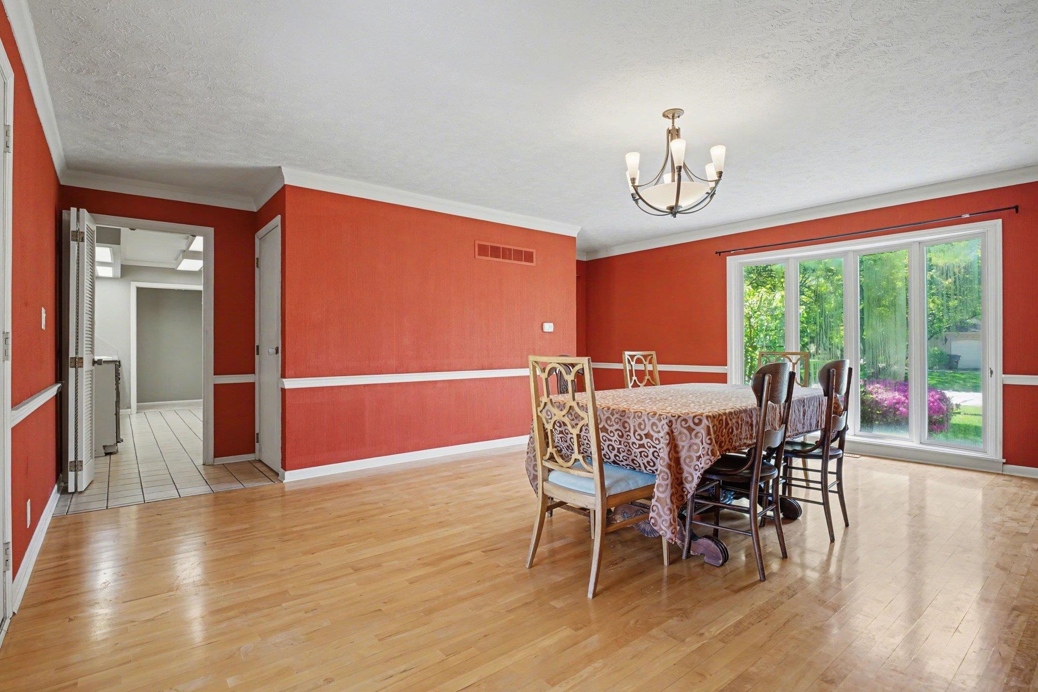 Dining area featuring wood-finish flooring, a contemporary ceiling fixture, crown molding, and sliding glass doors opening to outdoor greenery
