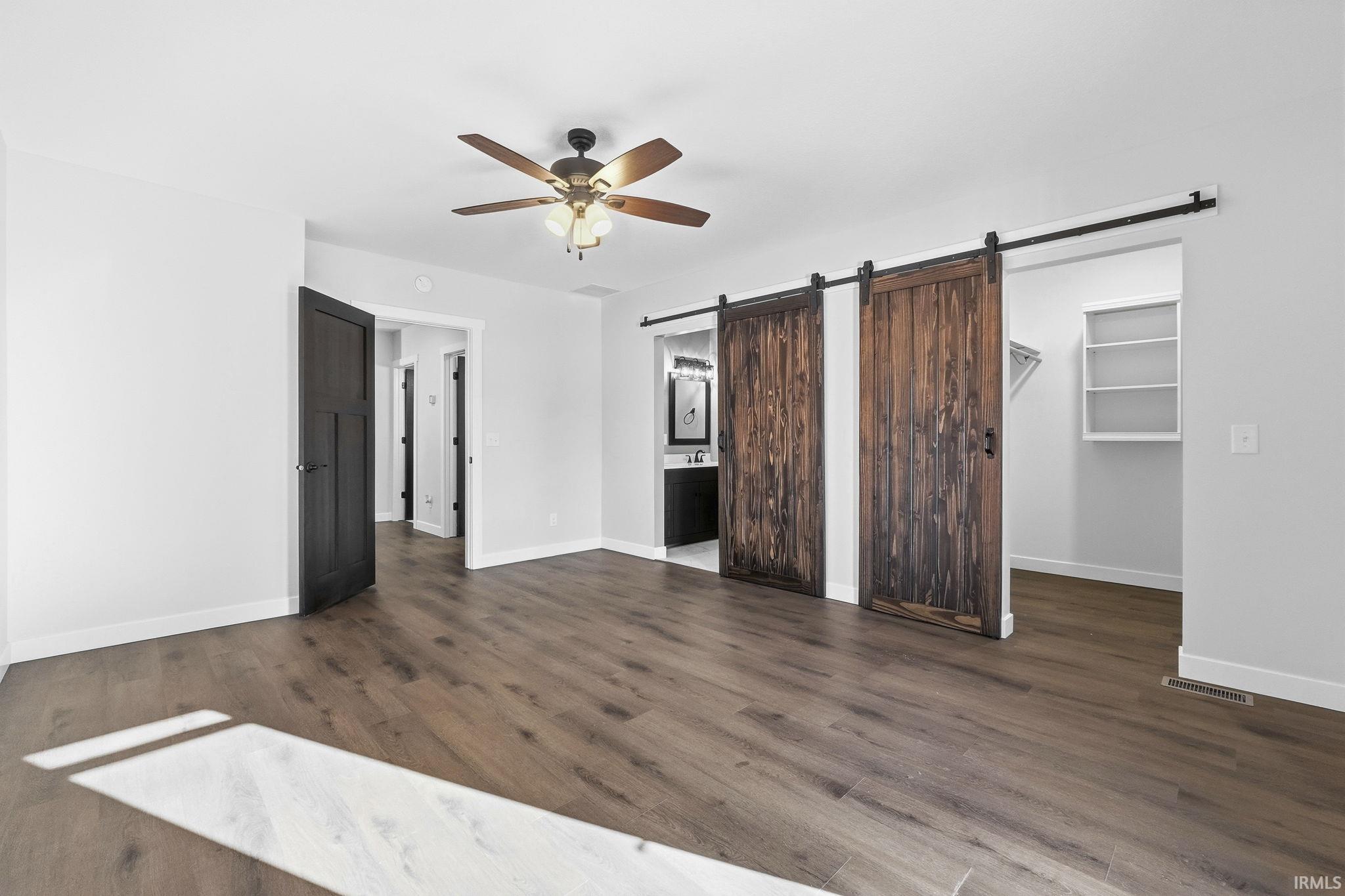 Unfurnished bedroom featuring a spacious closet, dark wood-type flooring, a barn door, and ceiling fan