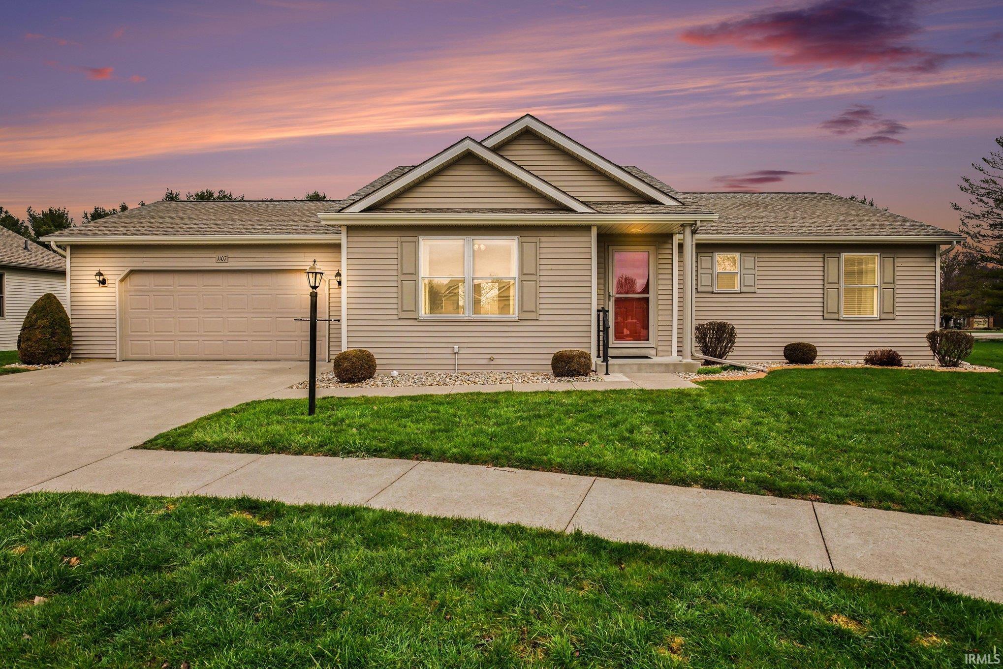 View of front of property featuring driveway, a yard, an attached garage, and roof with shingles