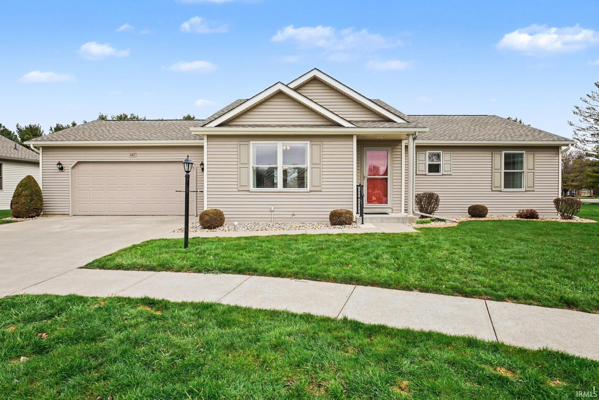 Ranch-style house featuring a shingled roof, concrete driveway, a front lawn, and an attached garage