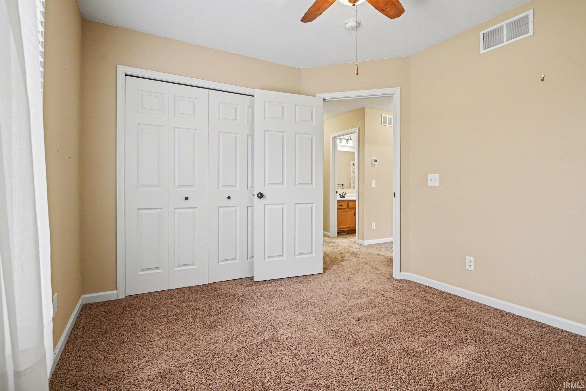 Unfurnished bedroom featuring light colored carpet, a closet, and a ceiling fan