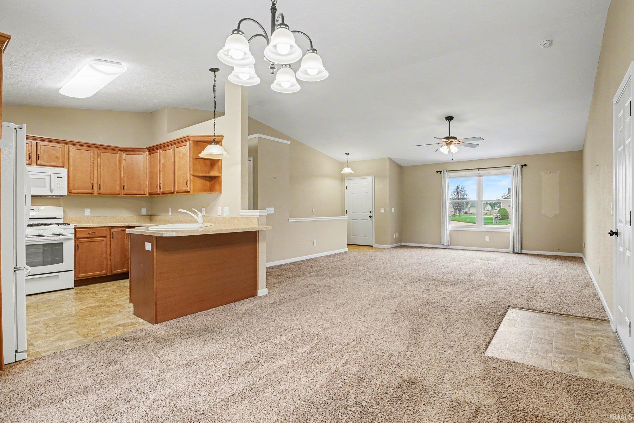 Kitchen with vaulted ceiling, light carpet, light countertops, open floor plan, and white appliances