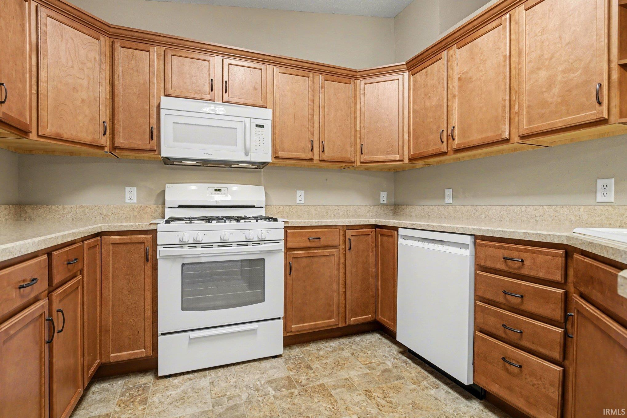 Kitchen with white appliances, wood finish cabinets, and stone finish floors