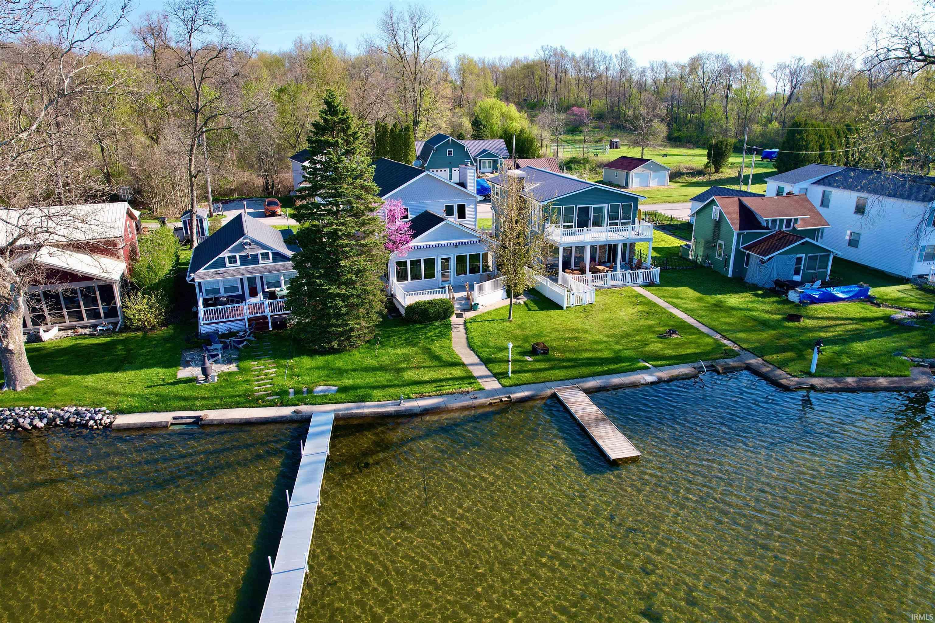 Waterfront property featuring a private dock extending into the lake, a manicured lawn, and mature trees