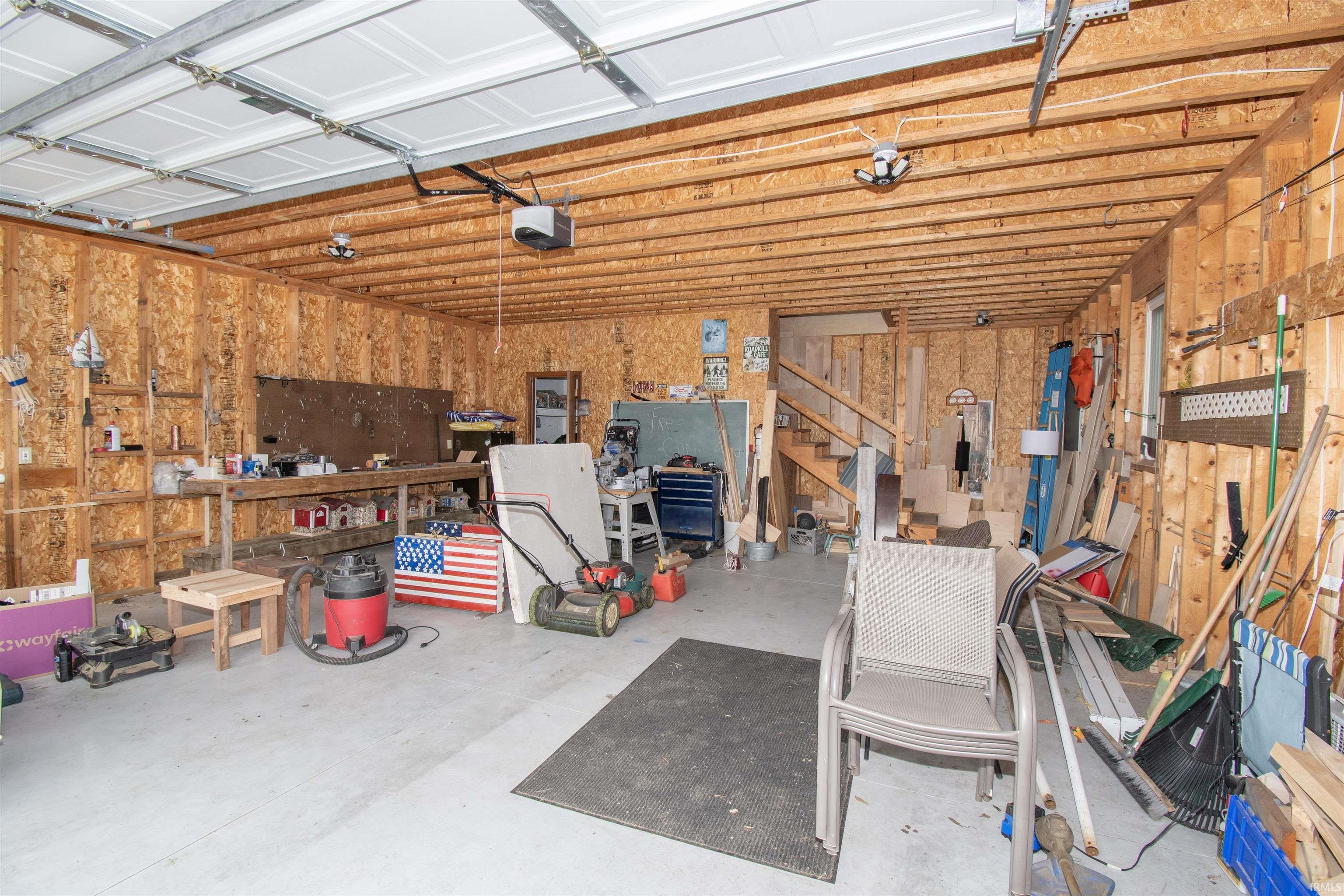 Spacious garage featuring exposed wood beam ceiling, concrete flooring, two garage door openers, and a visible staircase providing access to an upper level