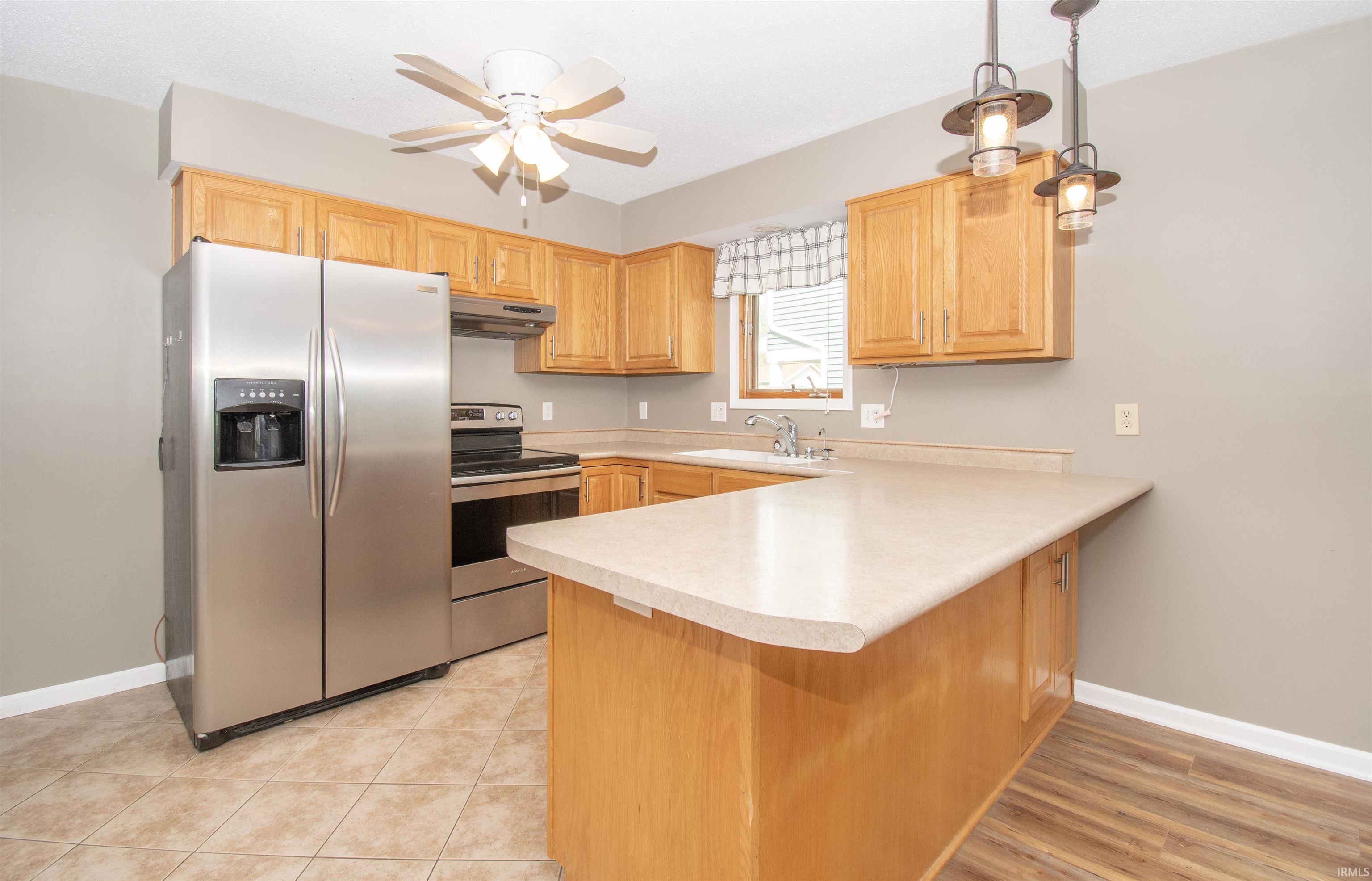 Kitchen featuring wood-finish cabinetry, stainless steel appliances, a light-toned countertop, a built-in breakfast bar, and mixed flooring with tile and wood-finish planks
