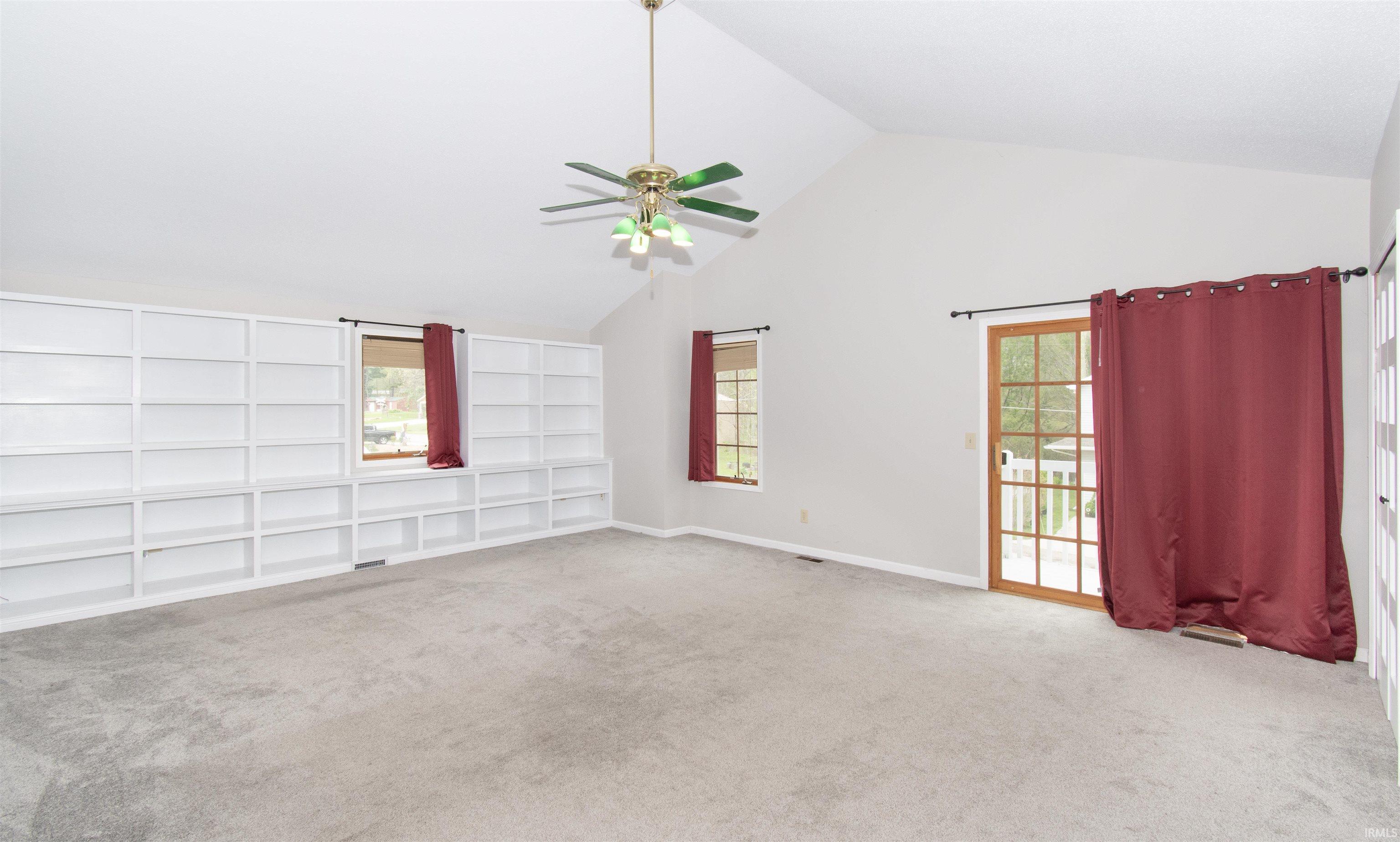 Spacious room featuring vaulted ceilings, built-in shelving, plush carpeting, and a ceiling fan